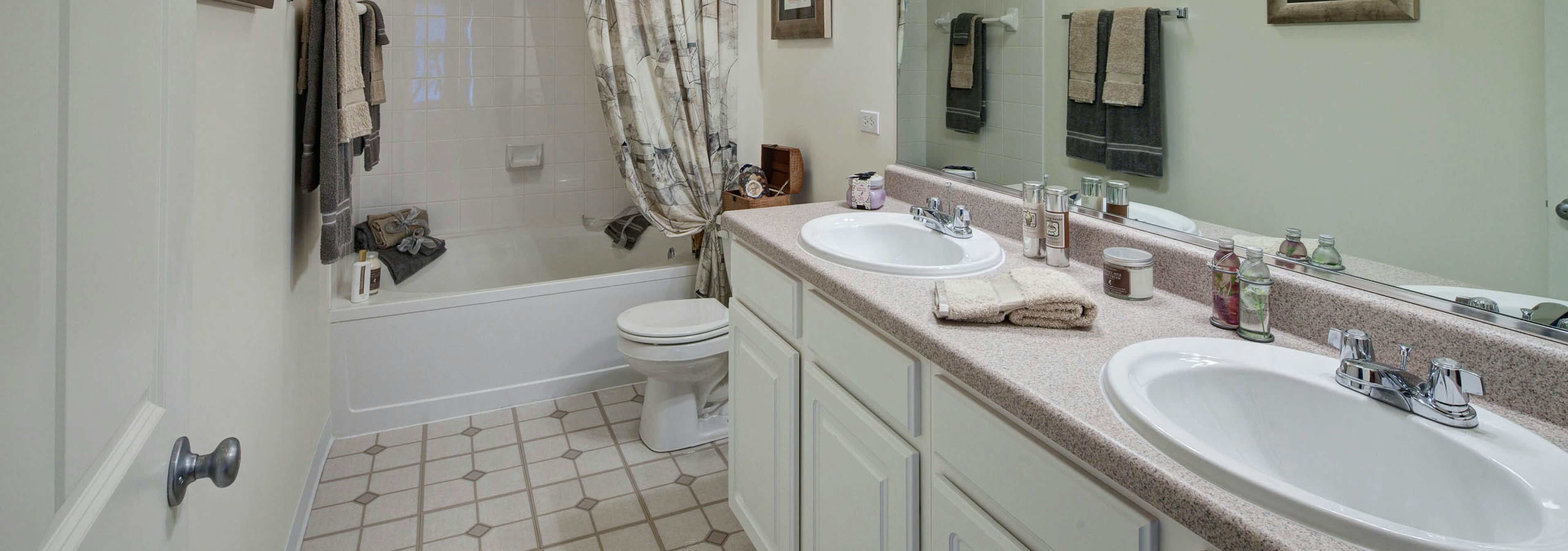 AMLI at Seven Bridges bathroom with a white double vanity next to a toilet with combined tub and shower and patterned floors