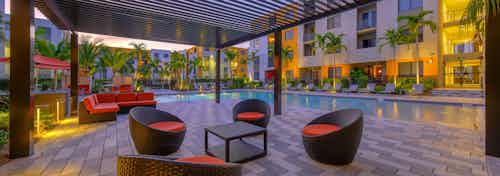 Outdoor vibrant orange seating area at AMLI 8800 with table and chairs poolside under pergola at dusk
