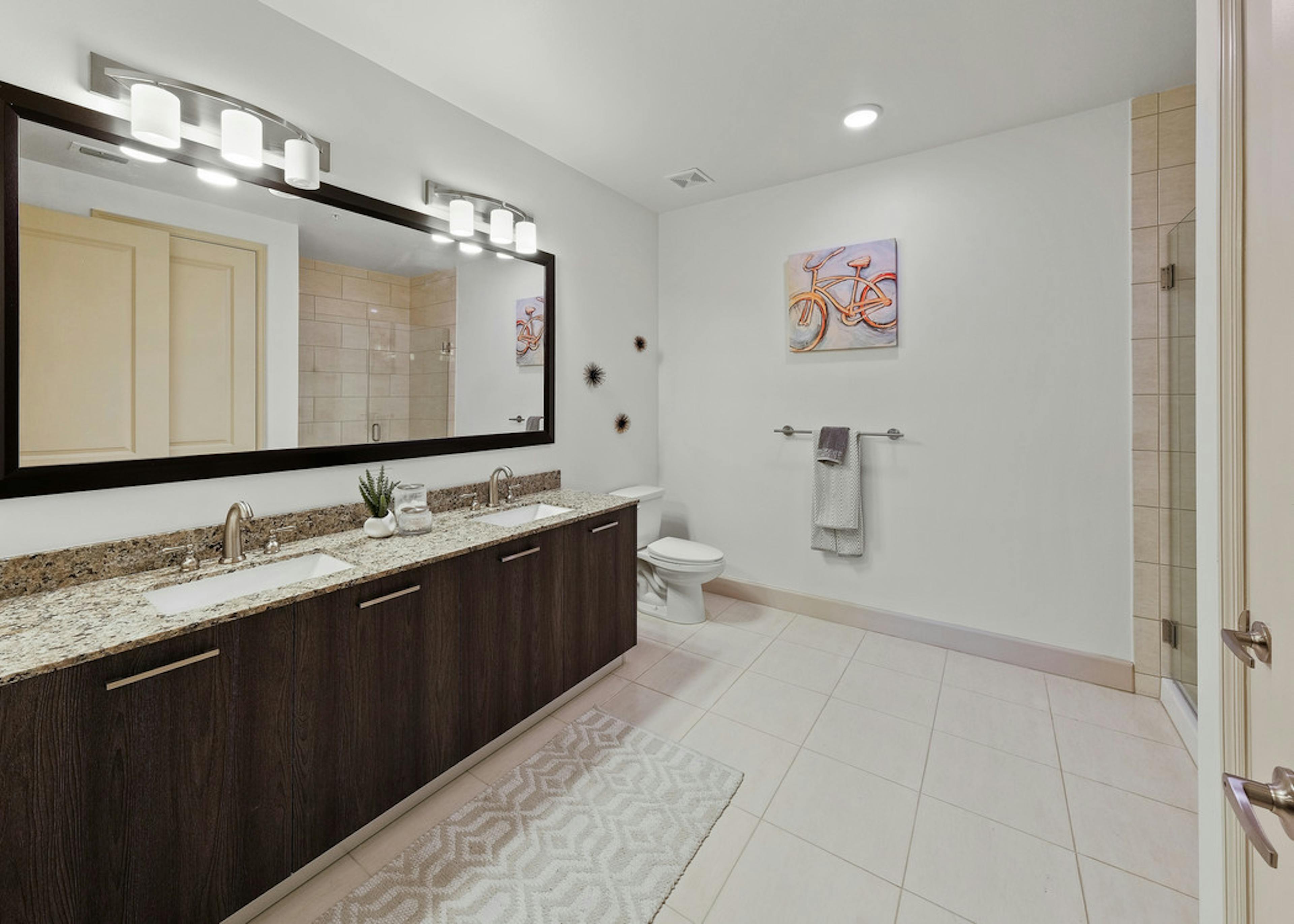 Interior view of AMLI 8800 apartment bathroom with double vanity, mirror, toilet and granite counters