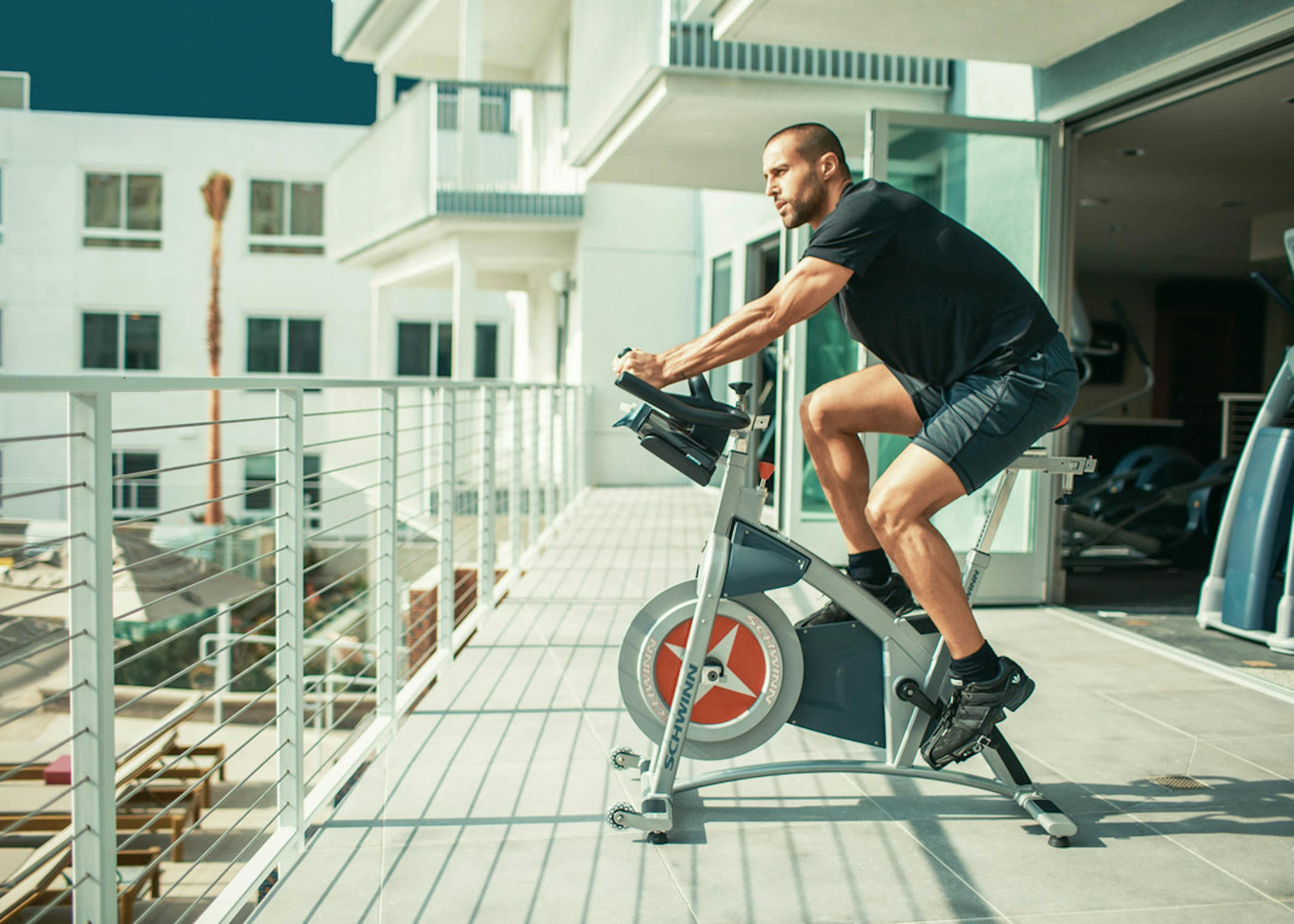 Daytime exterior view of man in shorts on spin bike on yoga deck overlooking the pool area at AMLI Lex on Orange apartments