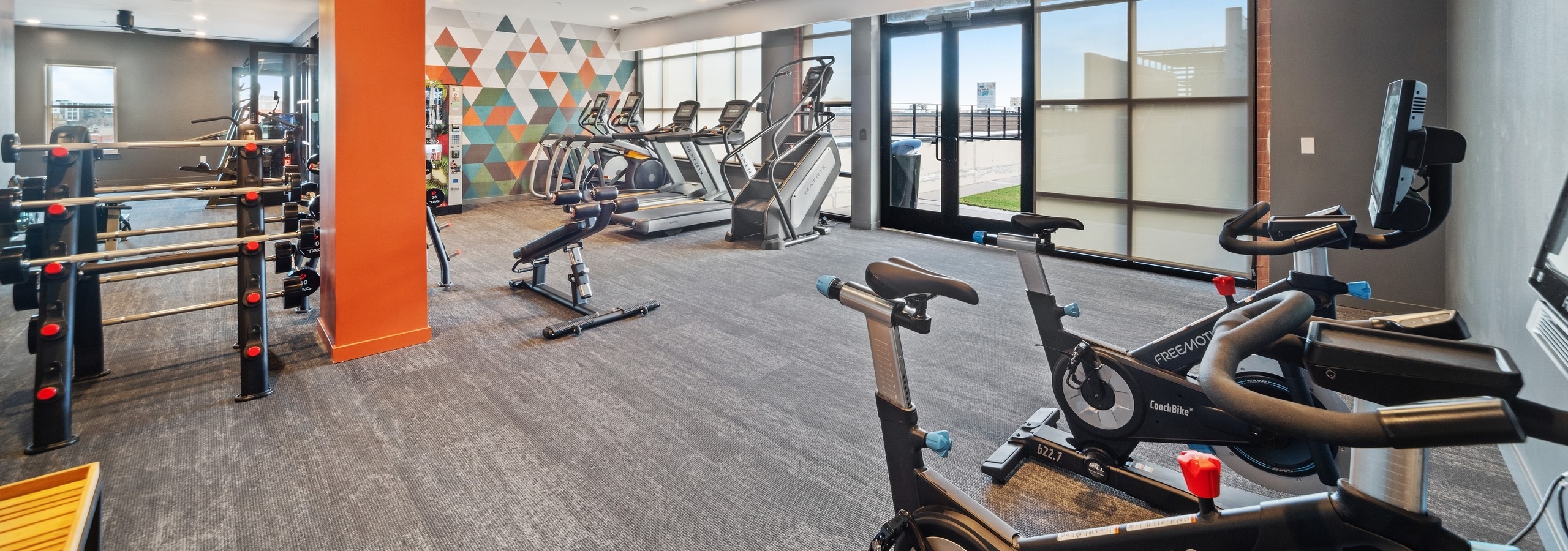 AMLI at Uptown fitness center with grey carpet flooring and floor to ceiling windows featuring a variety of exercise machines