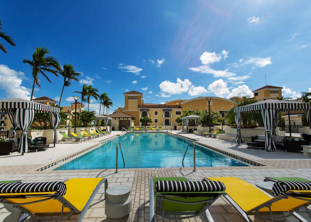 One of two swimming pools at AMLI Dadeland surrounded by lush palm trees, blue deck chairs and can be seen from the patios