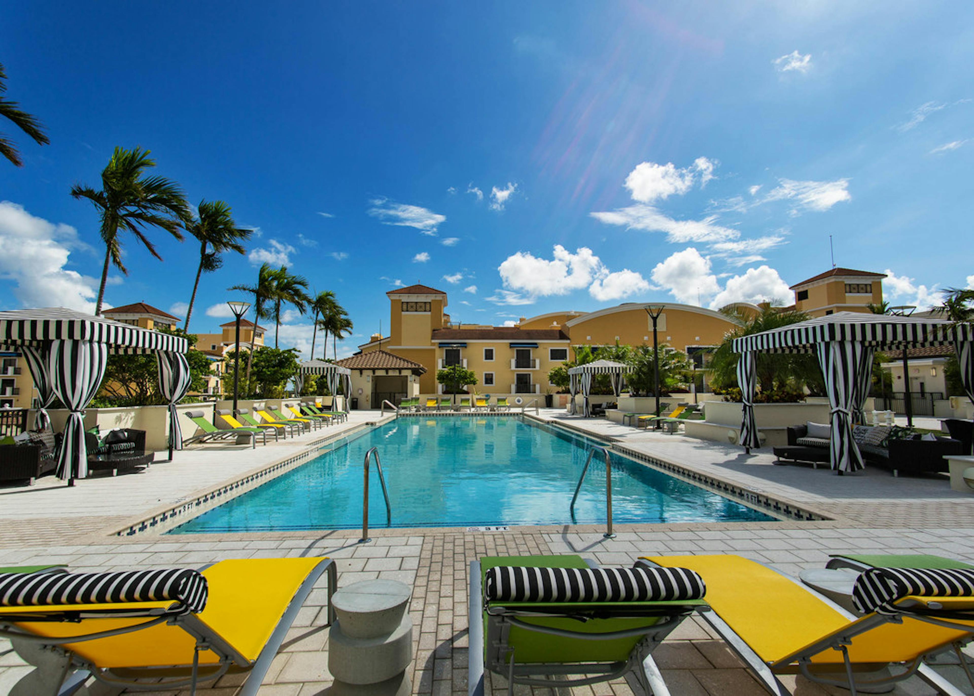 One of two swimming pools at AMLI Dadeland surrounded by lush palm trees, blue deck chairs and can be seen from the patios 