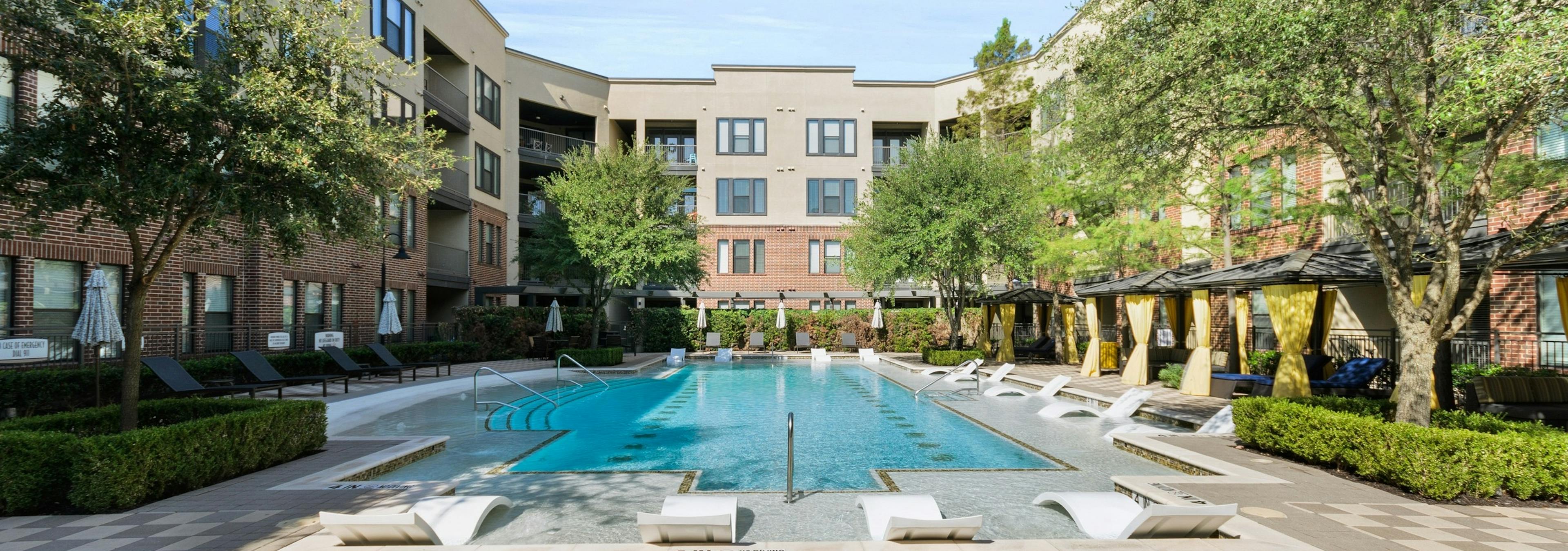 Daytime view of AMLI West Plano courtyard pool surrounded by gray lounge seating and cabanas with yellow privacy curtains