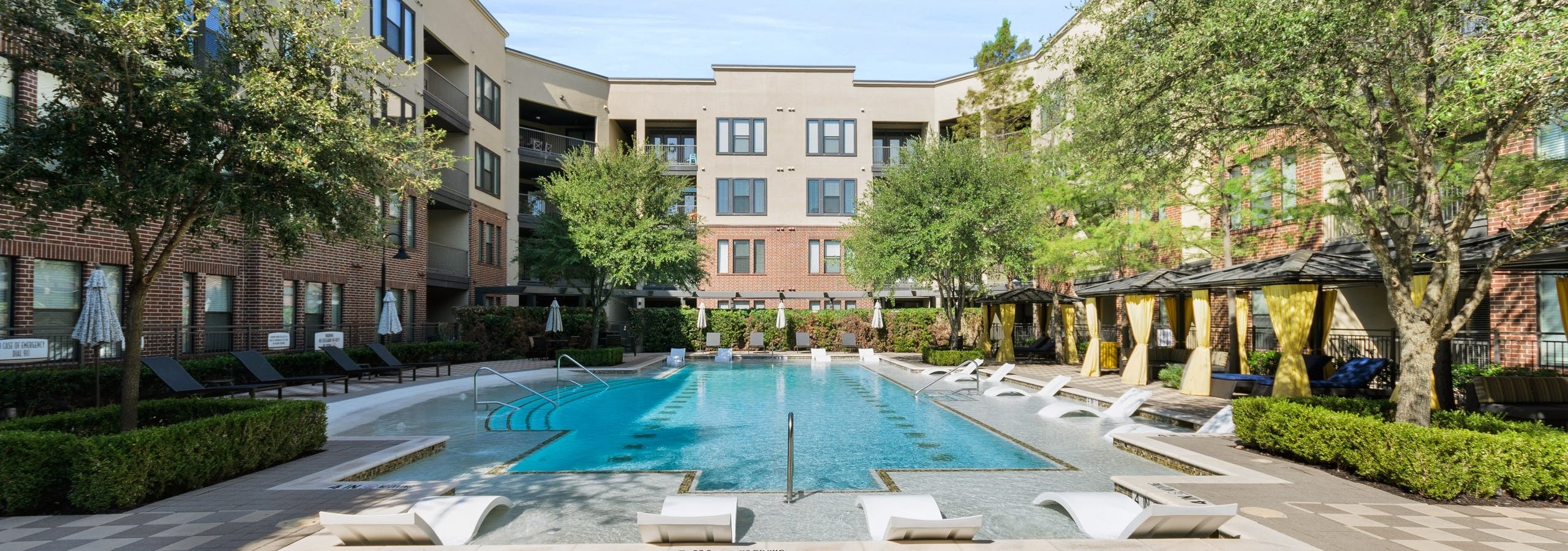 Daytime view of AMLI West Plano courtyard pool surrounded by gray lounge seating and cabanas with yellow privacy curtains