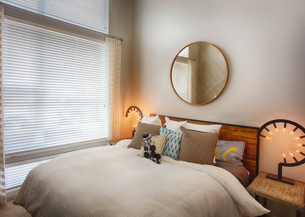 A bedroom at AMLI Denargo Market apartments featuring a bed with a wooden head board and a circular mirror and large window