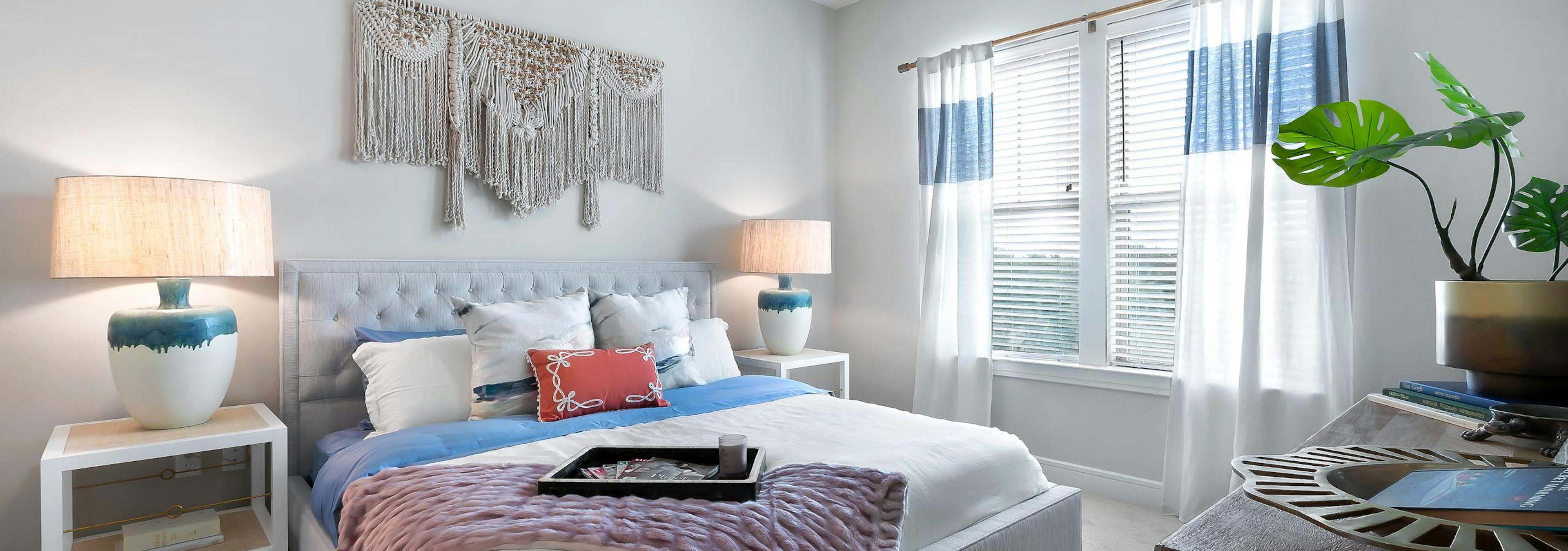 Bedroom at AMLI Lakeline apartments with large bed with colorful pillows and 2 nightstands with lamps and a large window