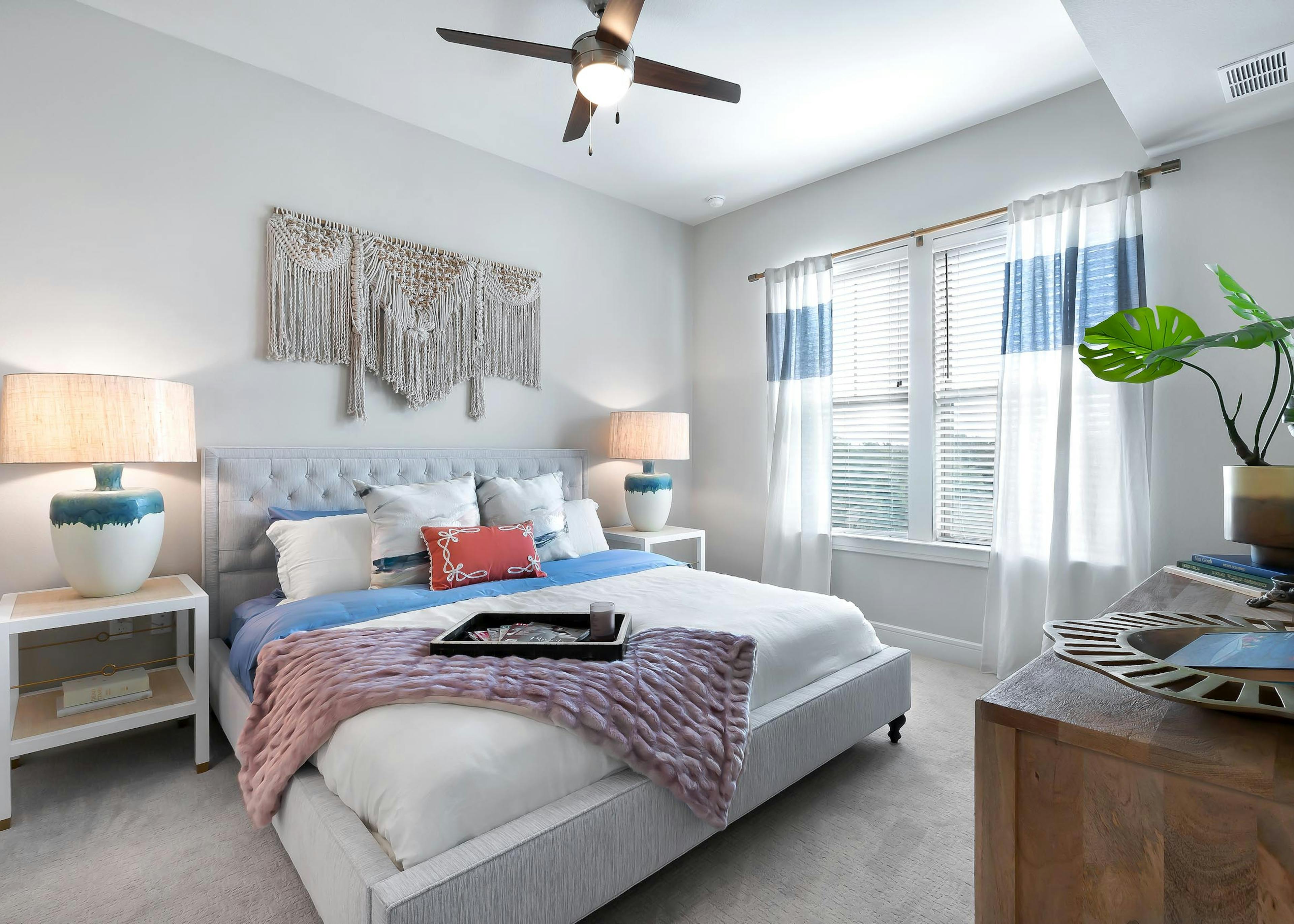 Bedroom at AMLI Lakeline apartments with large bed with colorful pillows and 2 nightstands with lamps and a large window