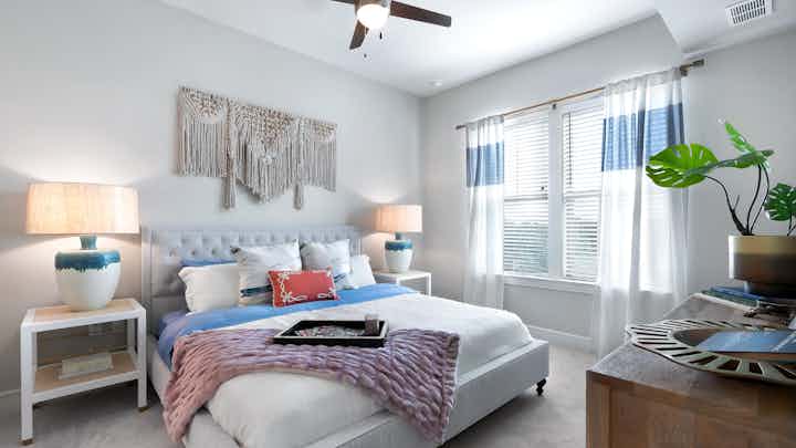 Bedroom at AMLI Lakeline apartments with large bed with colorful pillows and 2 nightstands with lamps and a large window