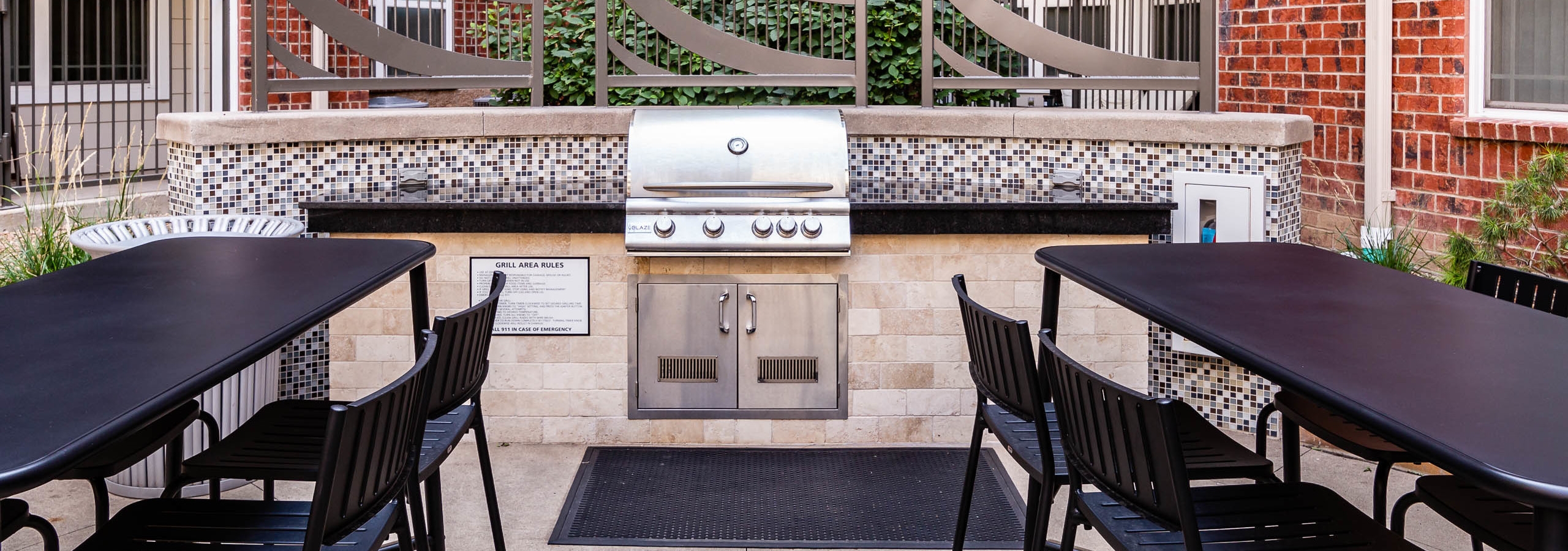 A barbecue area at AMLI Park Avenue apartments with a large surrounding counter top area and two black tables with chairs