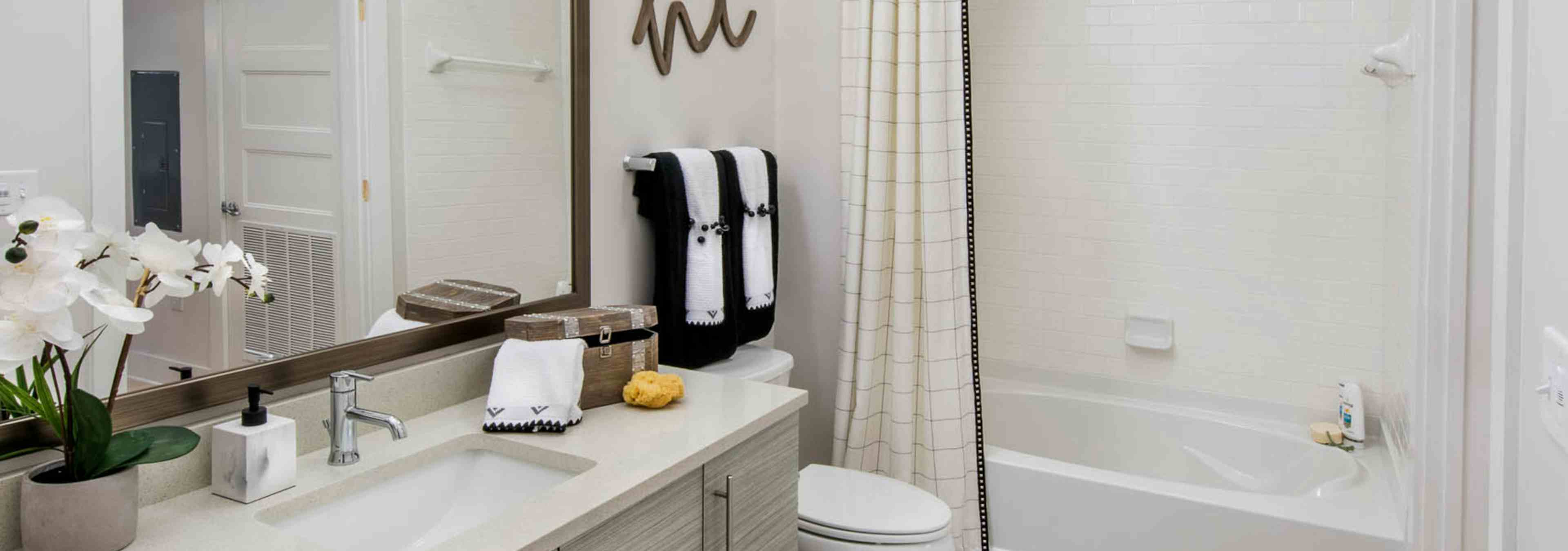 Bathroom at AMLI Buckhead with an orchid sitting on an ivory vanity countertop with a white combined bathtub and shower