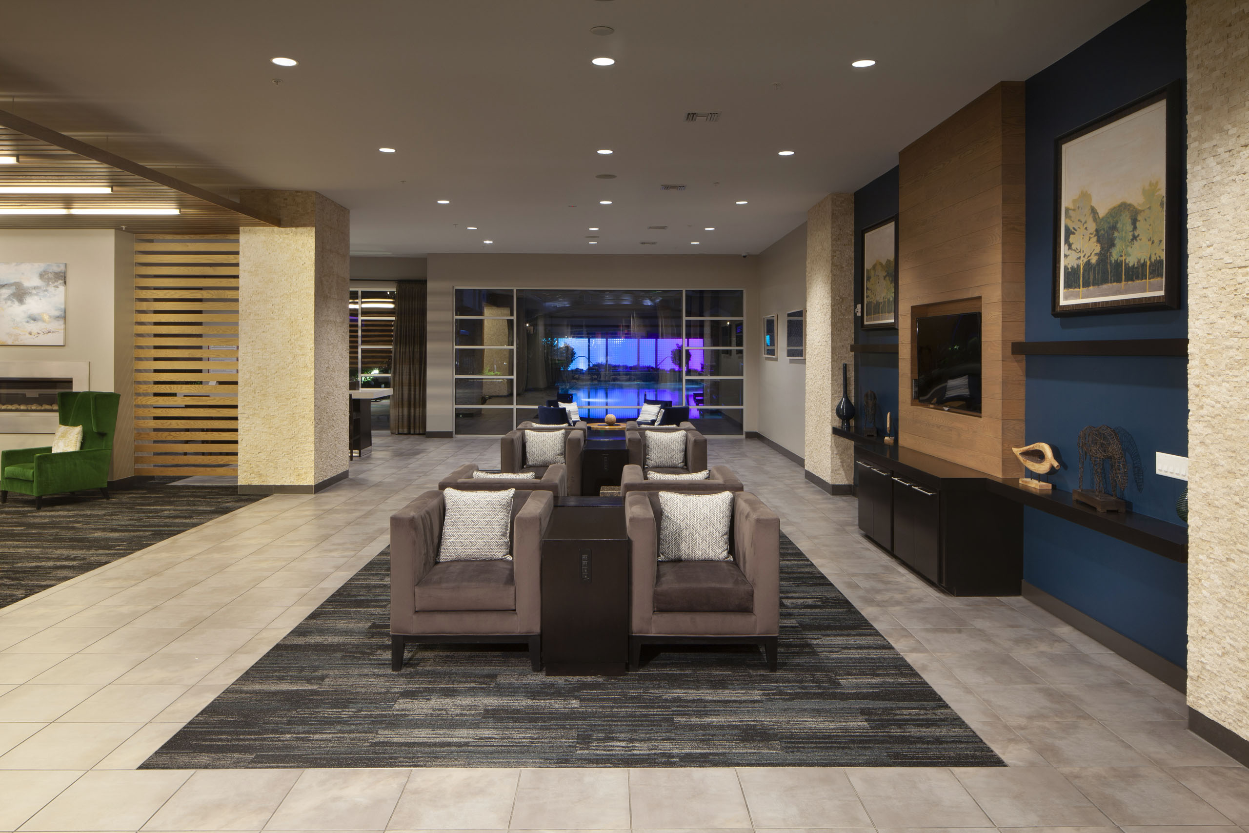Nighttime view of the clubroom with seating and artwork as well as a view of the pool with neon lights in the background