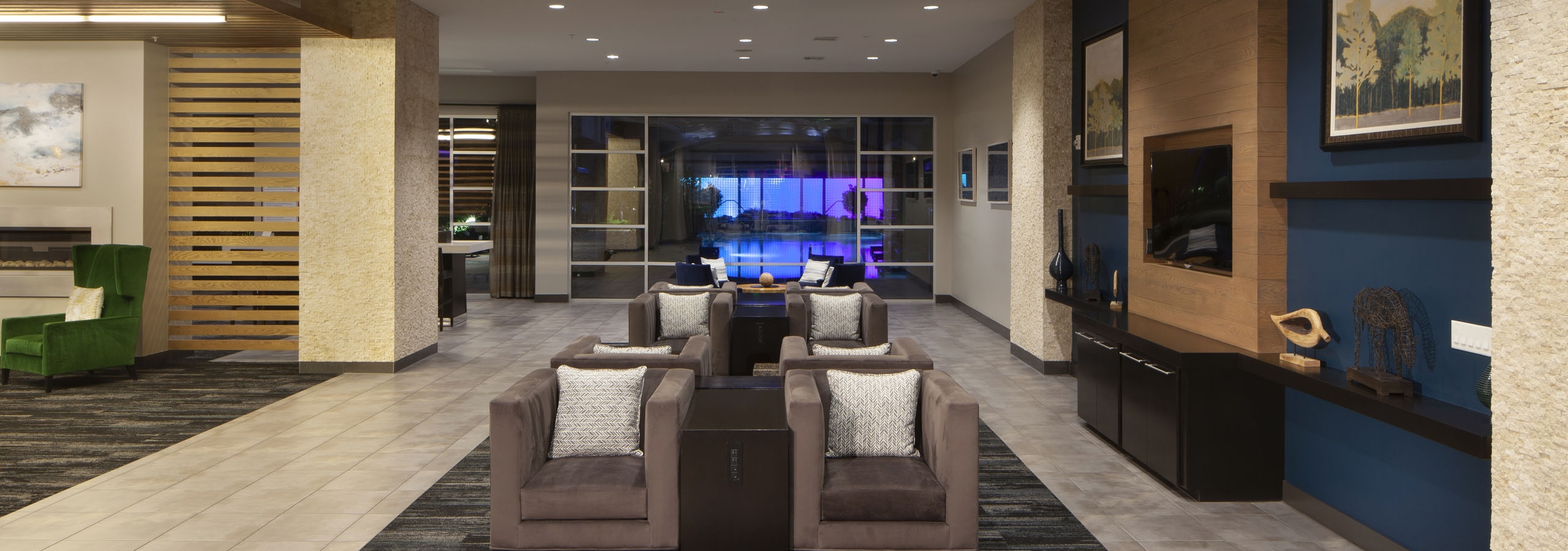 Nighttime view of the clubroom with seating and artwork as well as a view of the pool with neon lights in the background