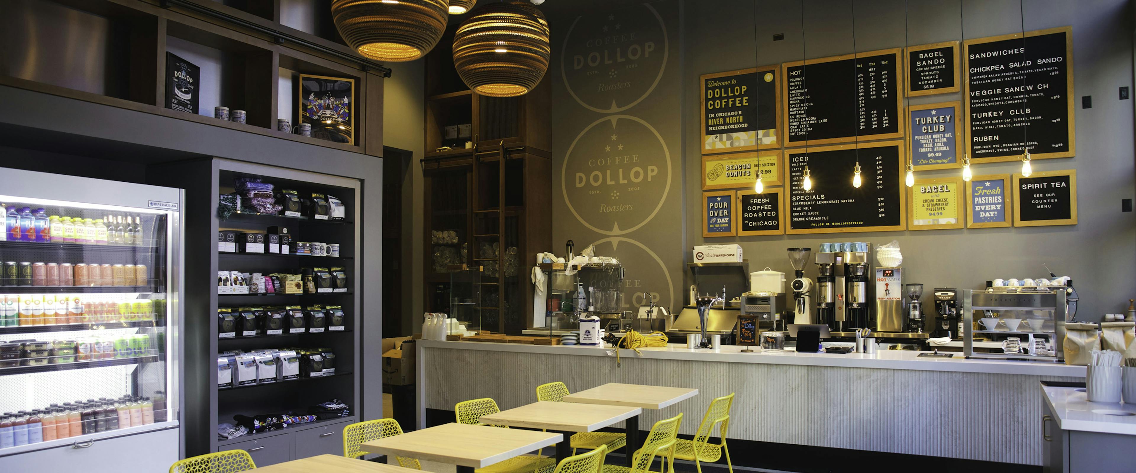 Interior view of Dollop coffee store at AMLI 808 apartment building with 4 tables and 8 yellow chairs and menu boards on wall