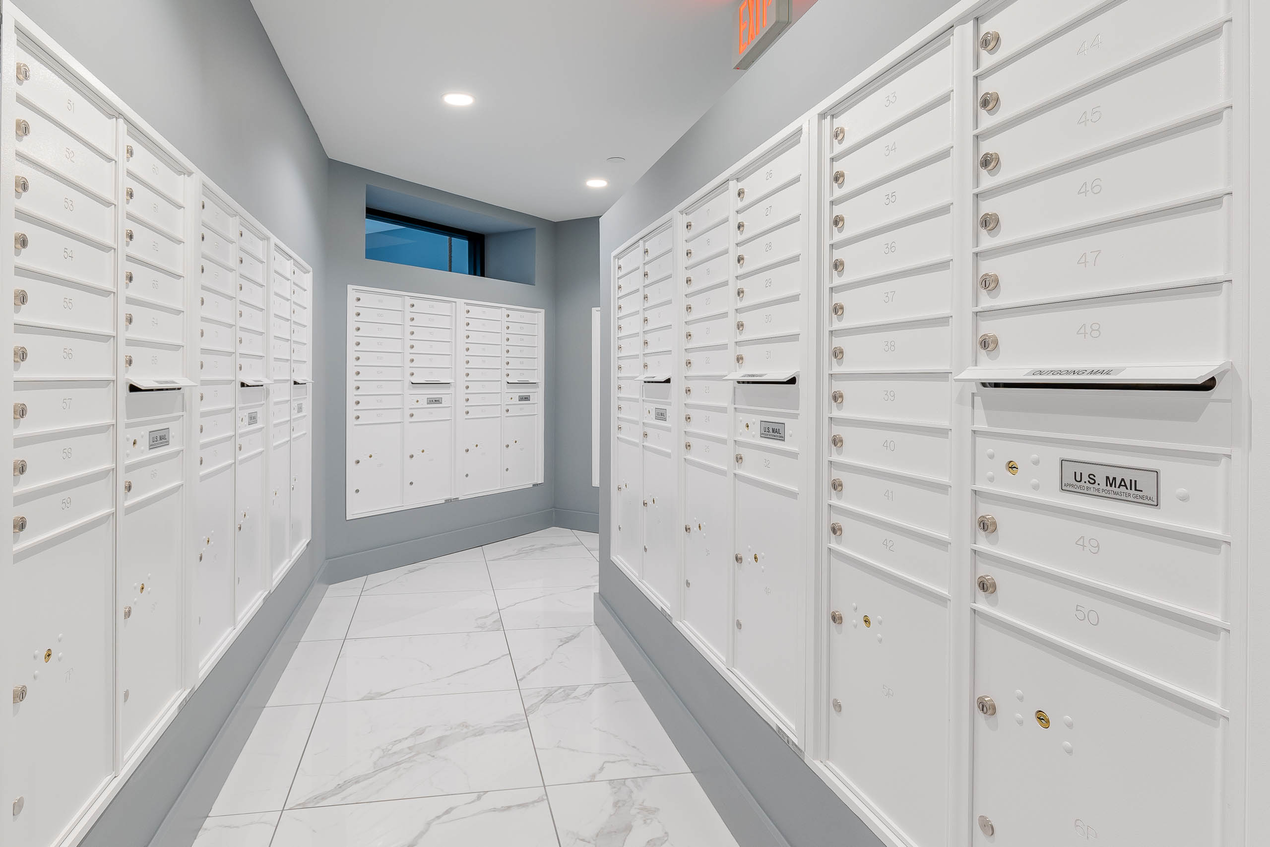 The mailroom at AMLI Park West apartment with marble tile floors and white mailboxes with light gray accent walls 