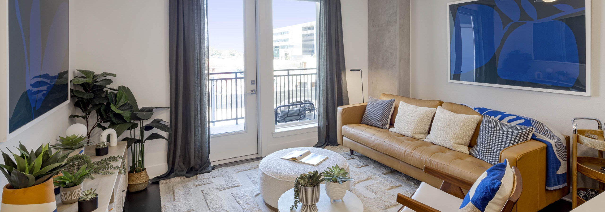 Living room with leather couch below blue artwork and grey curtains and view to exterior at AMLI Branch Park