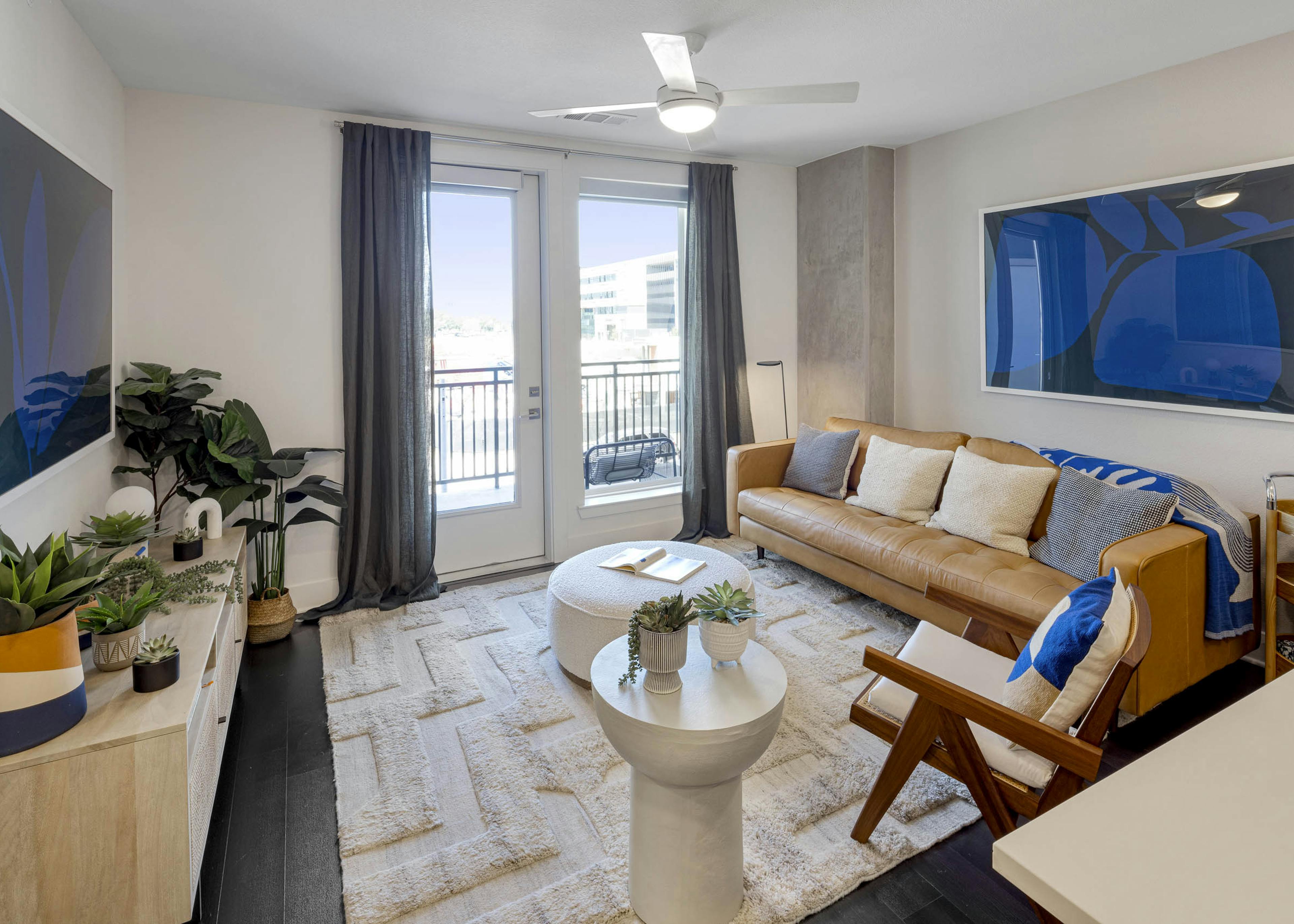 Living room with leather couch below blue artwork and grey curtains and view to exterior at AMLI Branch Park