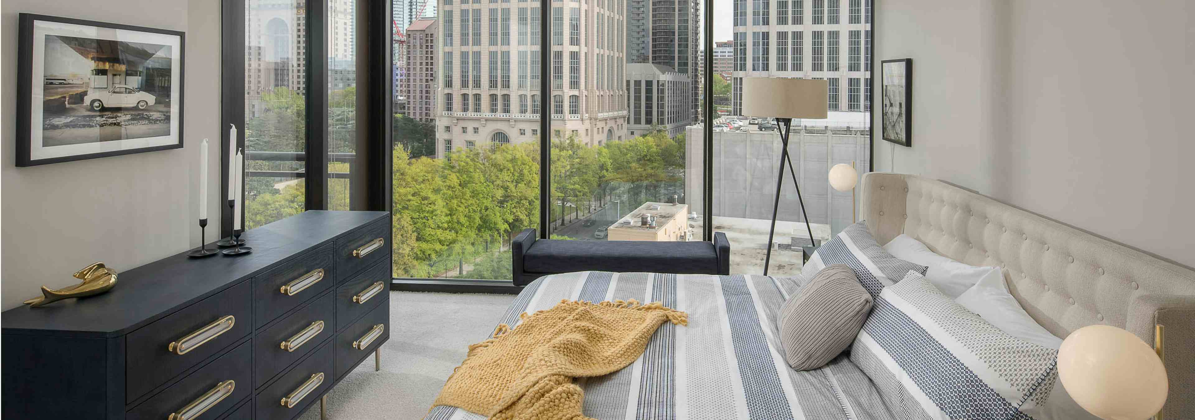 Bedroom at AMLI Arts Center with floor to ceiling windows and beige walls with striped bedding and white carpeted floors