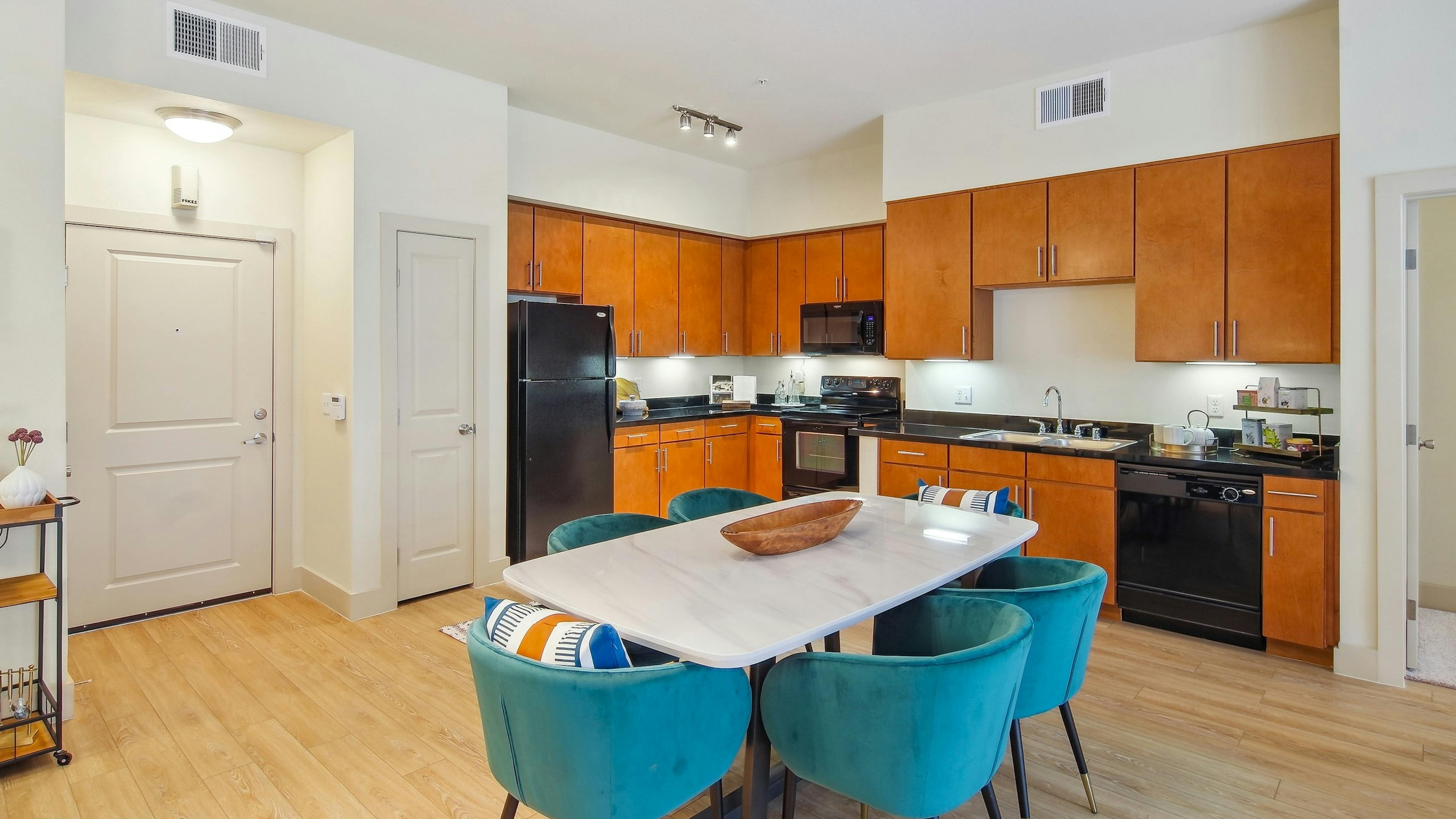 Kitchen and dining area at AMLI Park Avenue apartments with a long black countertop with wood cabinets and dining table