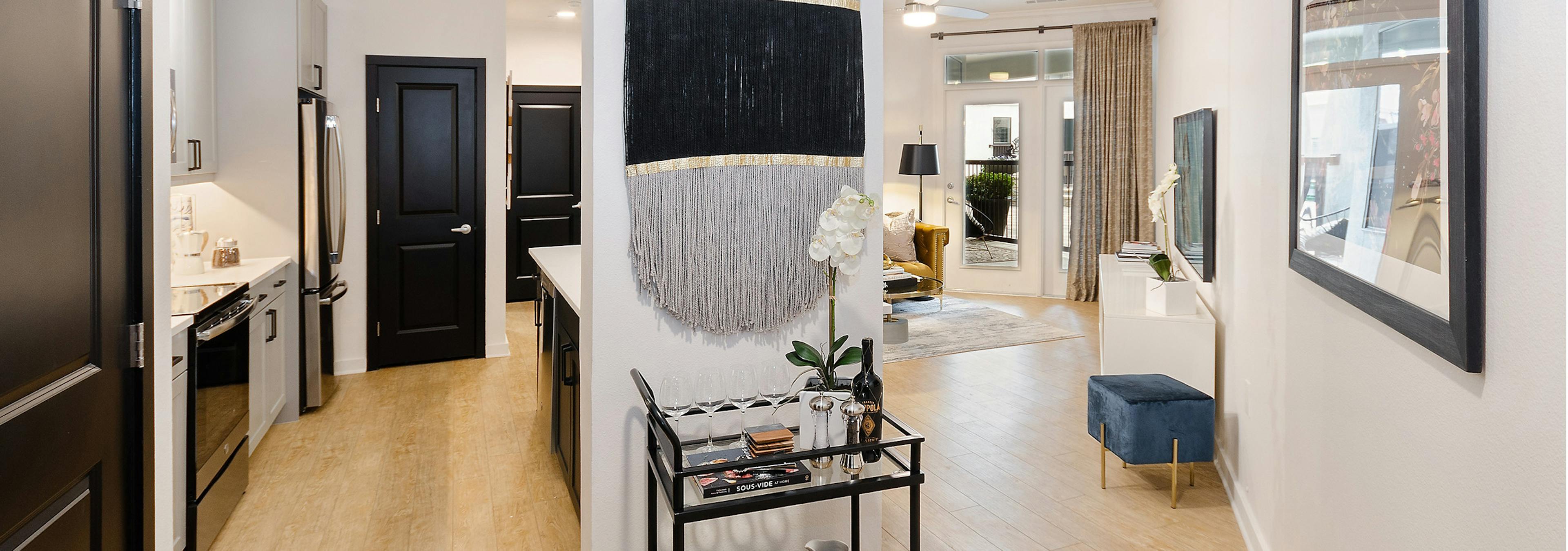 View of living room and kitchen at AMLI Quadrangle with light harwood and neutral walls with black and grey decor