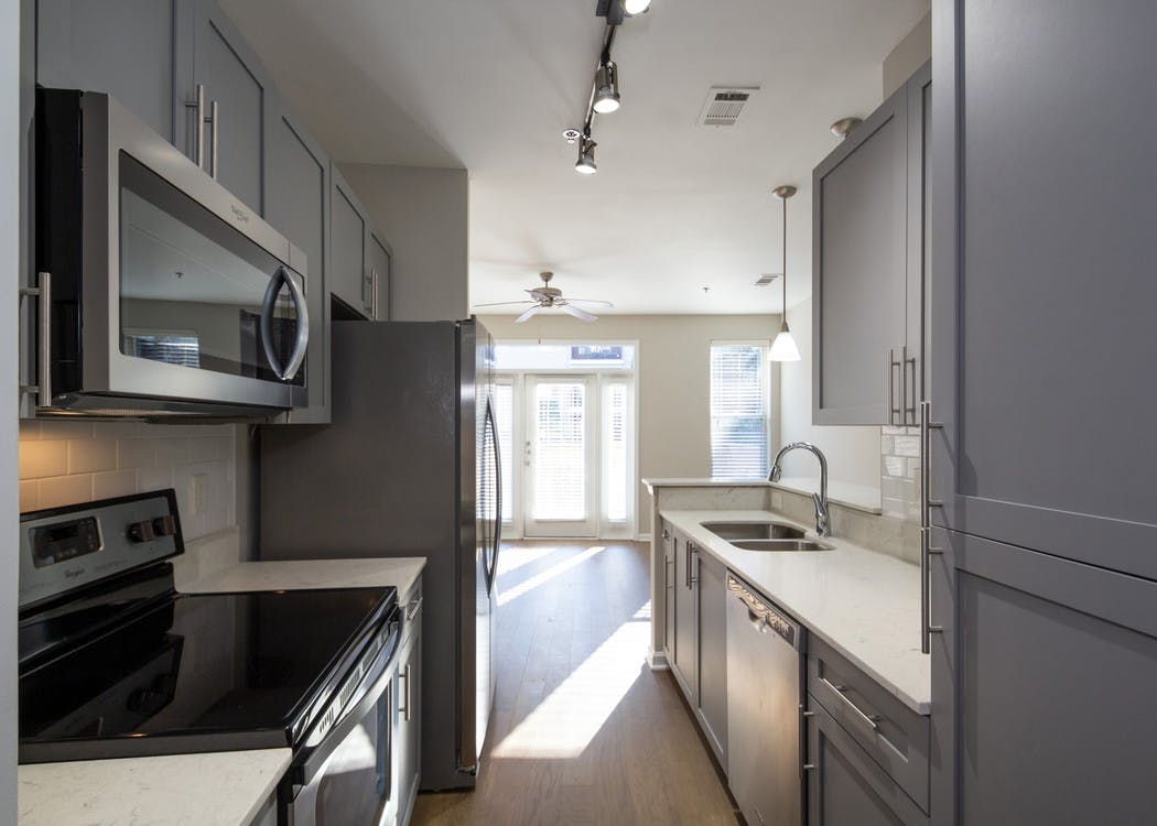 Interior view of AMLI Lindbergh apartment kitchen with grey cabinets and white countertops with stainless steel appliances