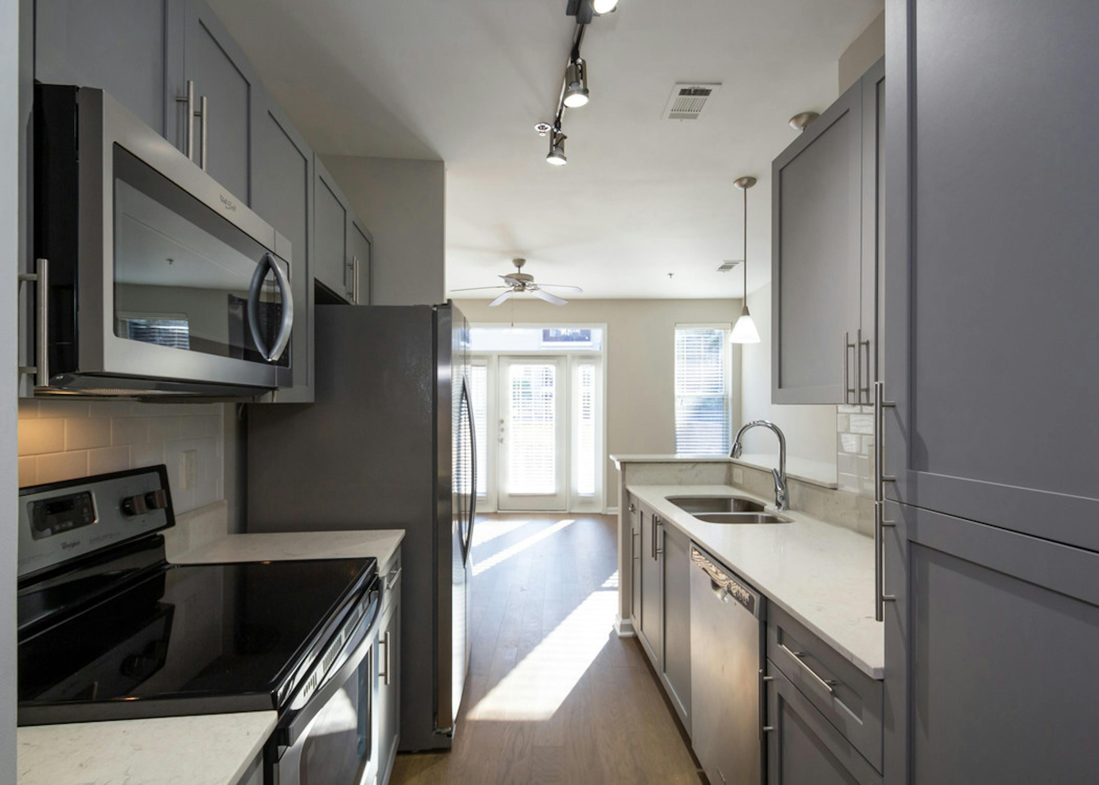 Interior view of AMLI Lindbergh apartment kitchen with grey cabinets and white countertops with stainless steel appliances