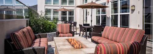 A rooftop fire pit at AMLI Park Avenue apartments with surrounding couches and tables and umbrellas and lush green plants