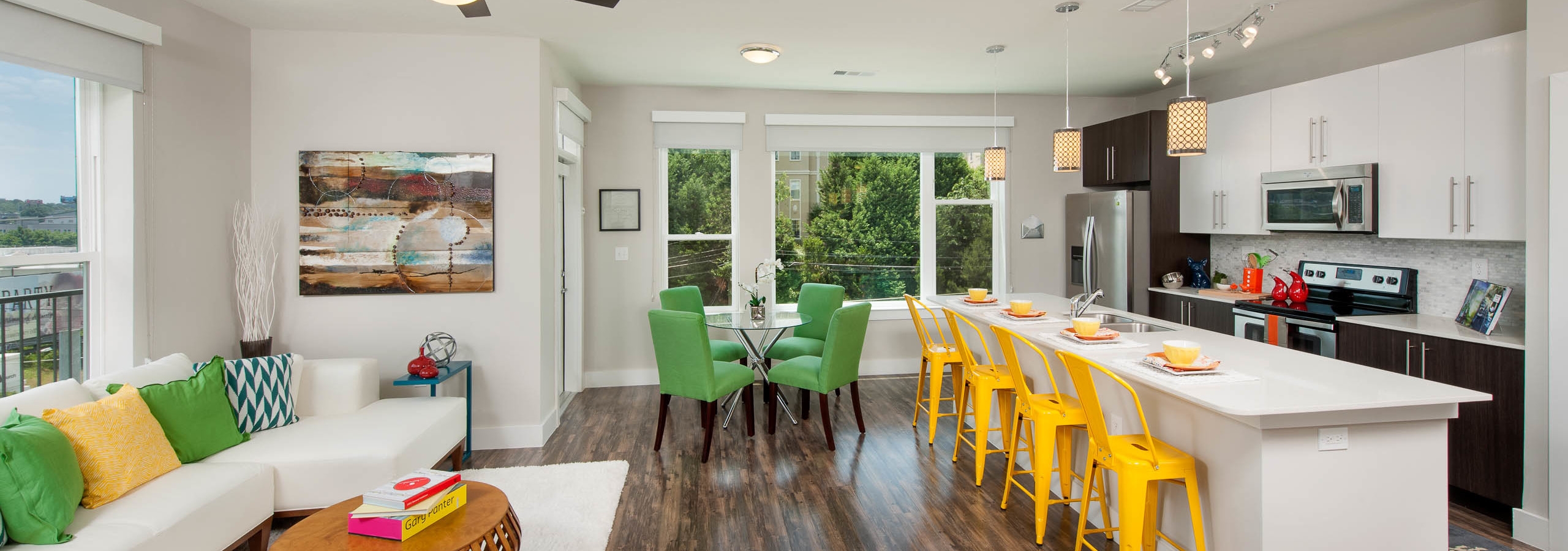 AMLI Piedmont Heights kitchen and living room with medium wood floors and long quartz countertop island with yellow barstools