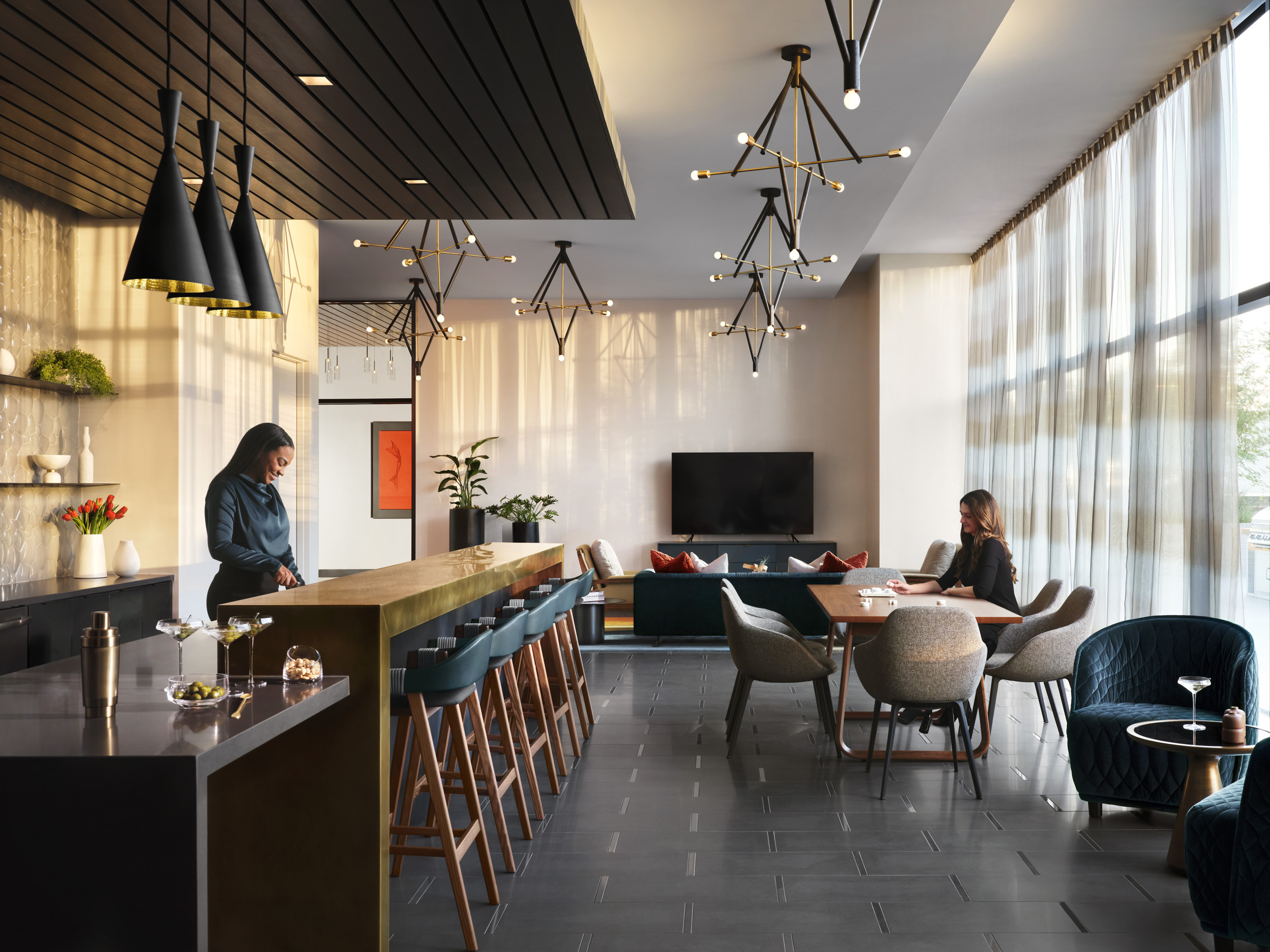 Resident lounge at AMLI Fountain Place apartments with woman behind bronze counter with stools and other seating nearby