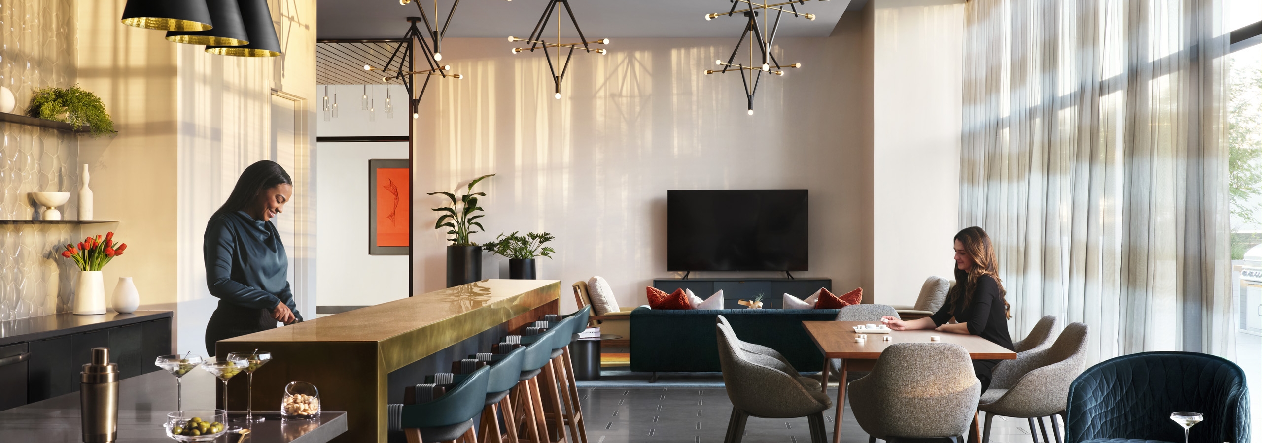 Resident lounge at AMLI Fountain Place apartments with woman behind bronze counter with stools and other seating nearby