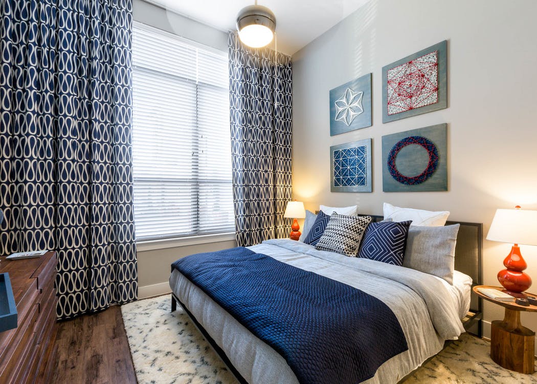 AMLI on Riverside bedroom with blue and grey bed against a creme wall with a large window with patterned curtains to the left