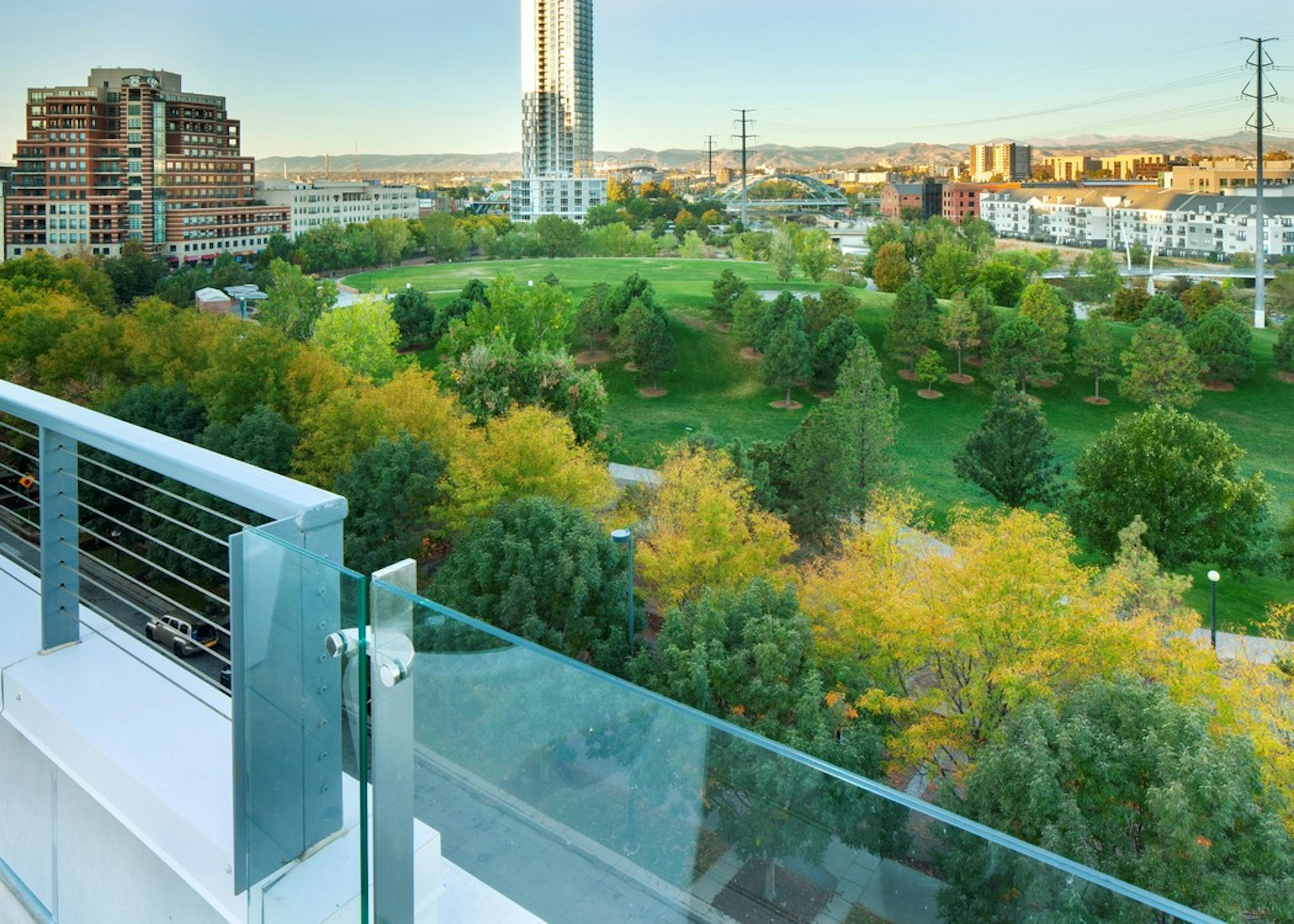 Exterior view from rooftop deck at AMLI Riverfront Green apartments with a park with several green trees adjacent buildings 