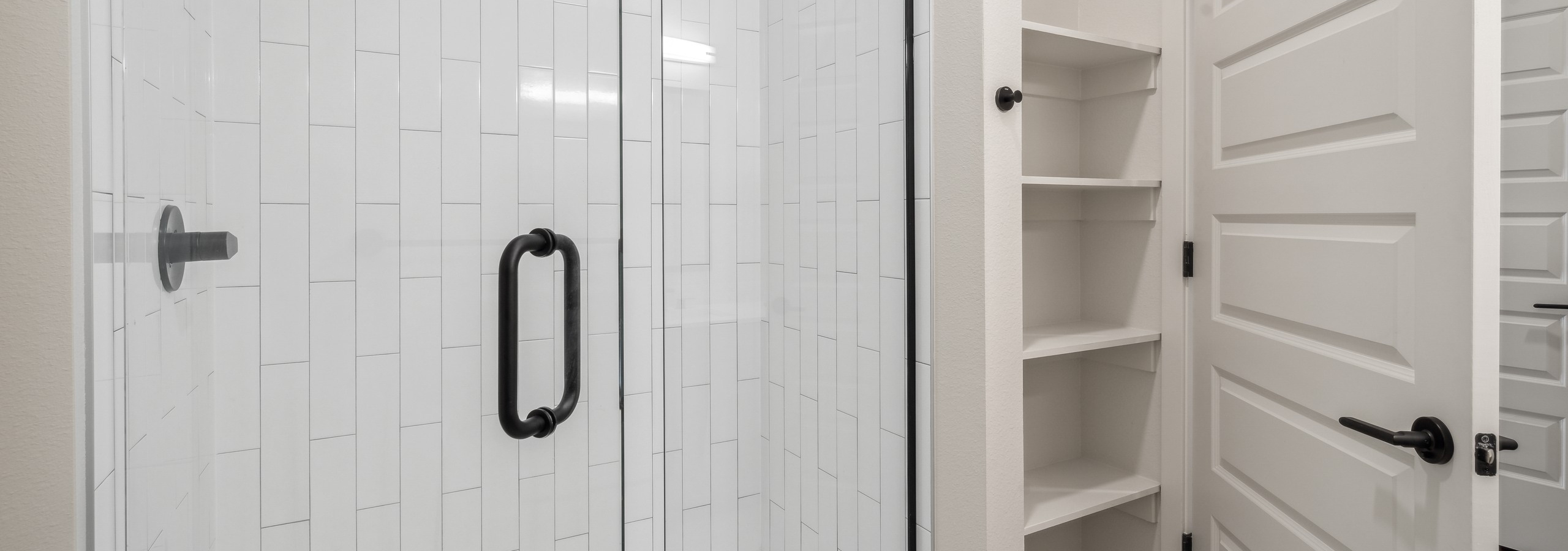 AMLI Broadway Park bathroom with glass enclosed white tile shower and linen closet with shelves and white door