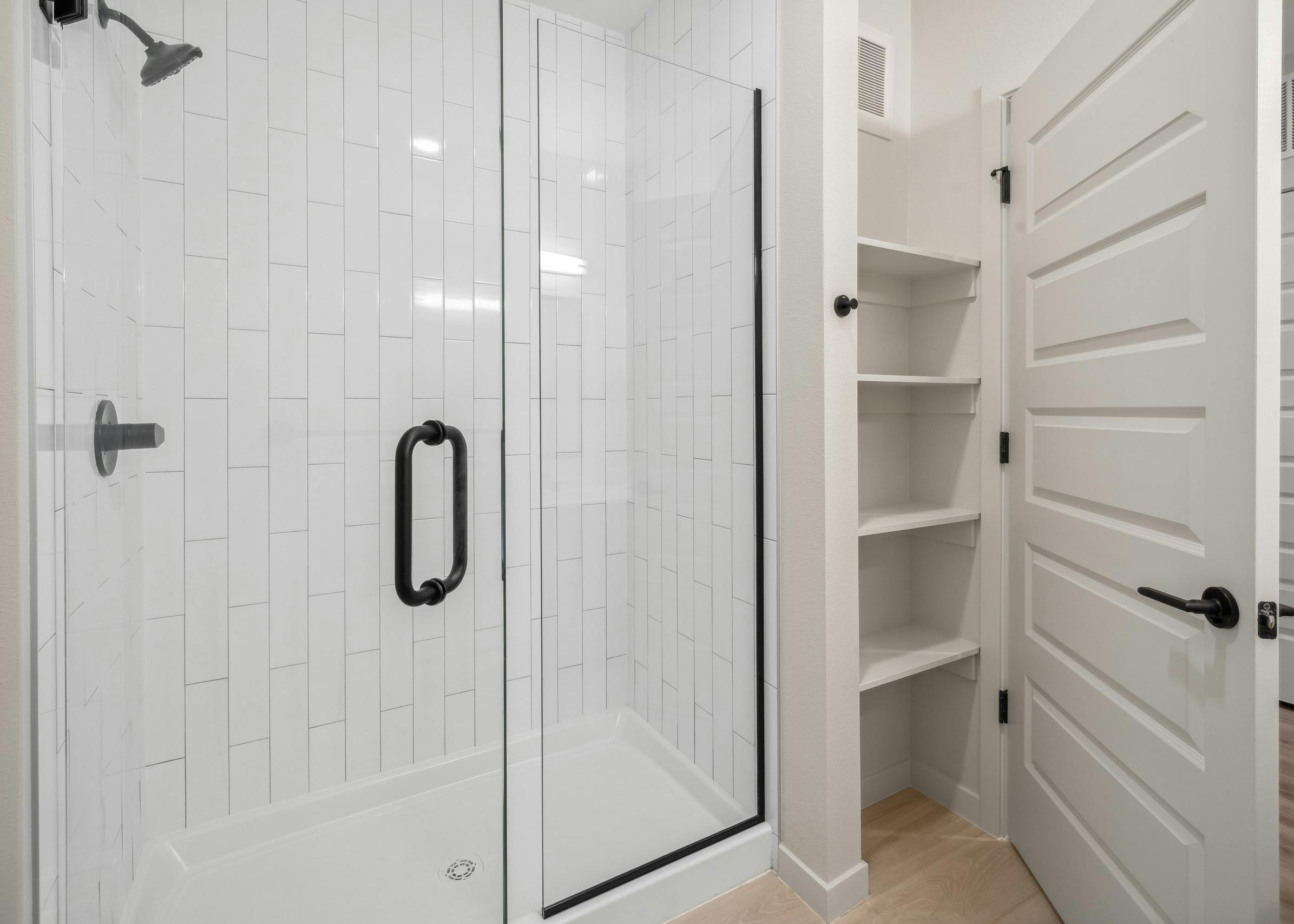AMLI Broadway Park bathroom with glass enclosed white tile shower and linen closet with shelves and white door