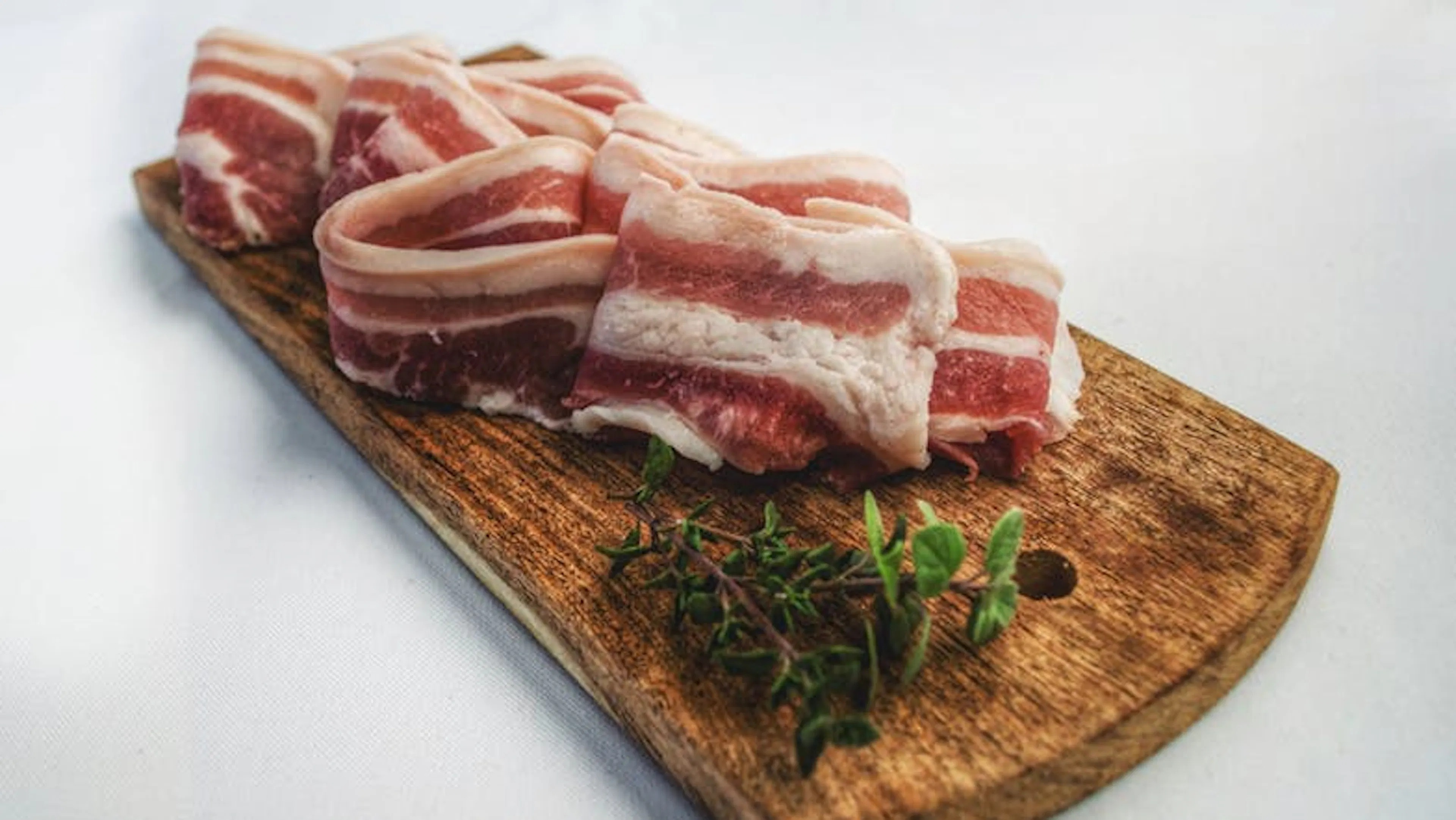 Slices of bacon on a rustic wooden cutting board with sprigs of thyme