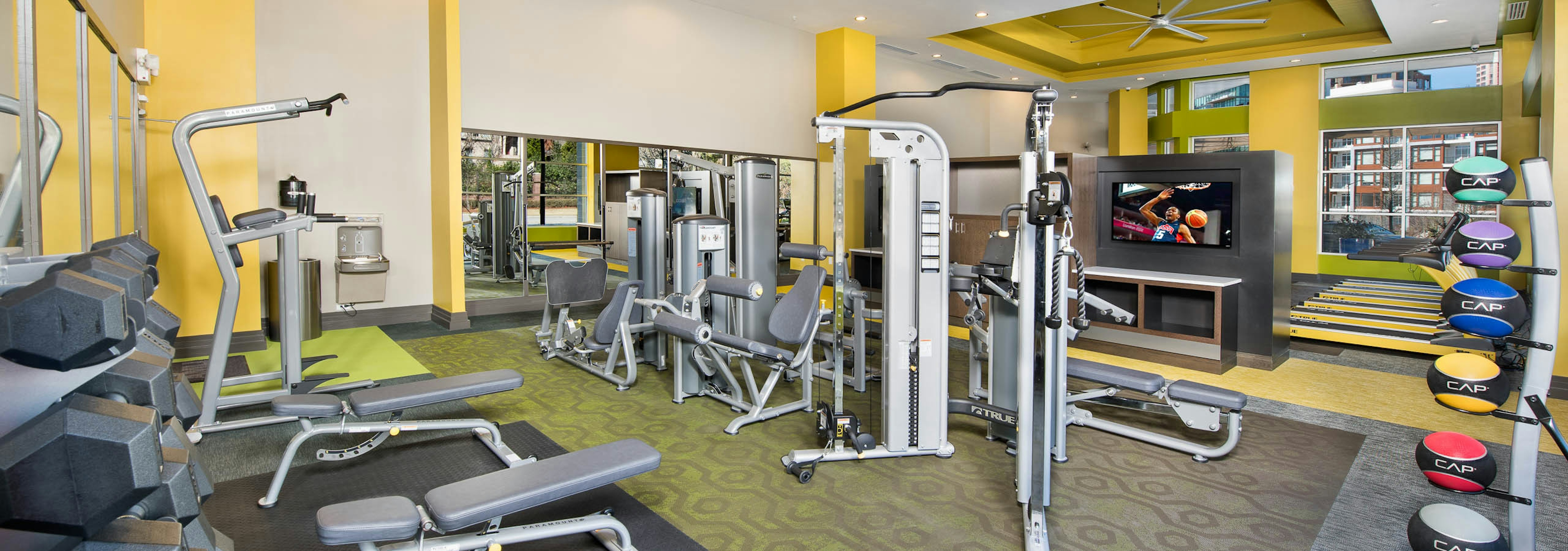 Interior of spacious AMLI Buckhead fitness center with a variety of weight machines with yellow walls and grey flooring