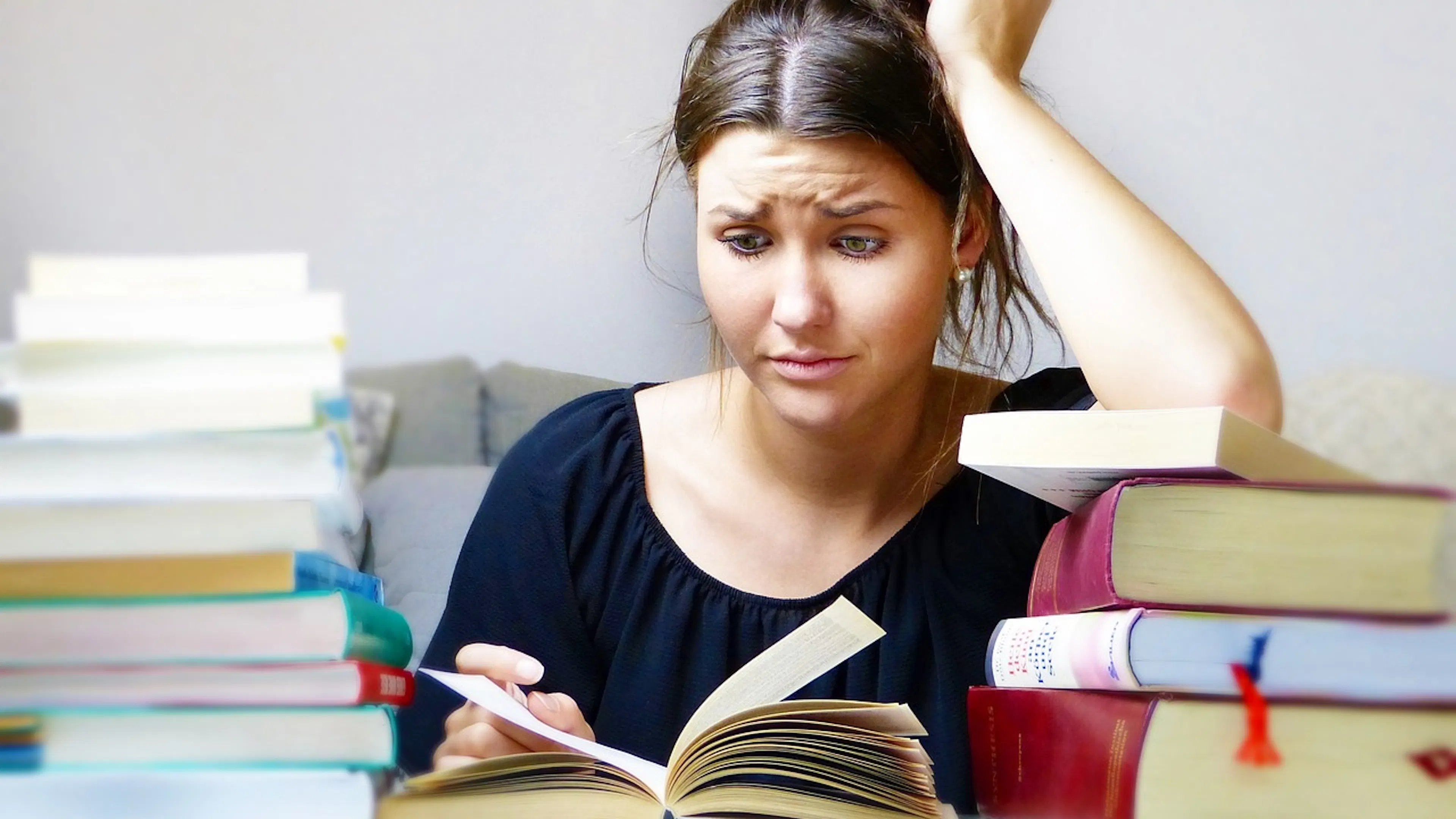A woman sitting among a pile of books while looking overwhelmed and stressed