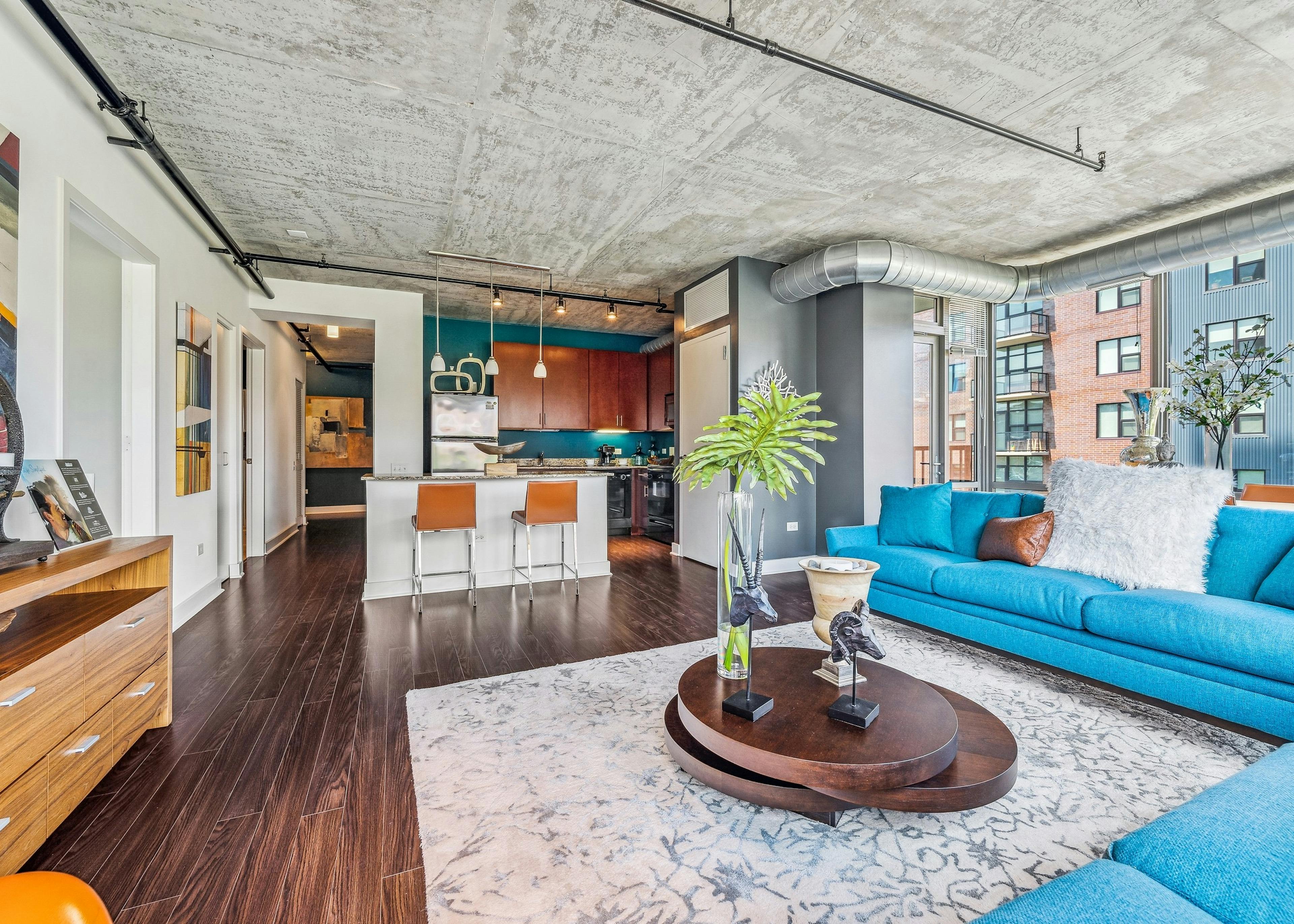 Living room with blue couches and round wood coffee table with cream and grey rug and distressed ceiling and large window