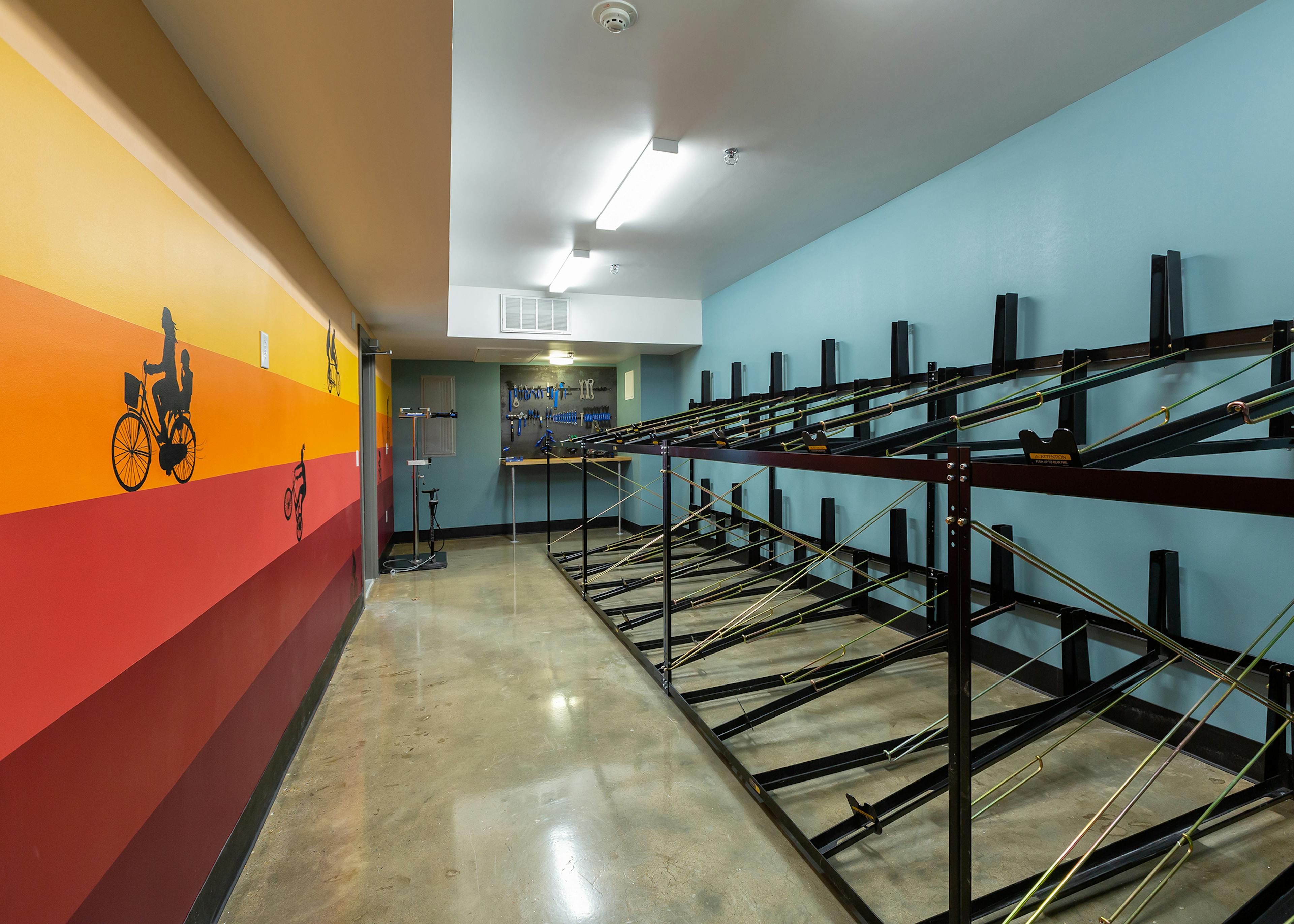 Interior view of bike room at AMLI South Shore apartments with empty bike racks and colorful walls and repair station in rear