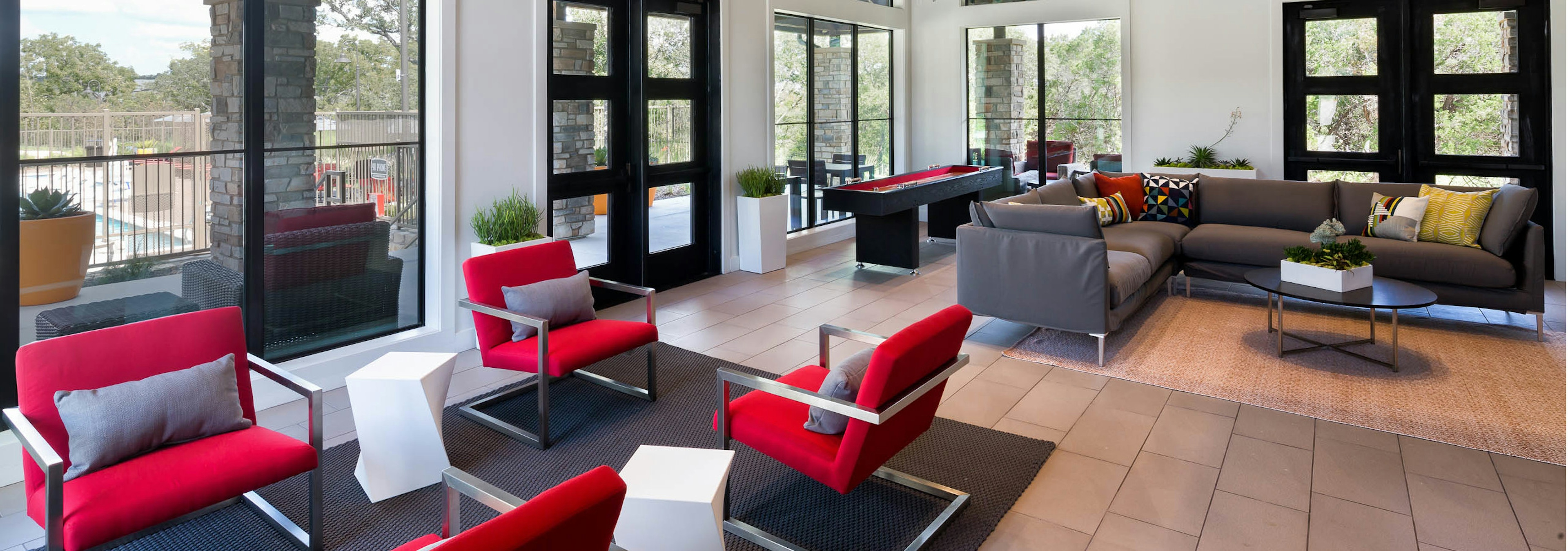 Daytime view of AMLI Covered Bridge resident game room with red and gray seating and shuffleboard table