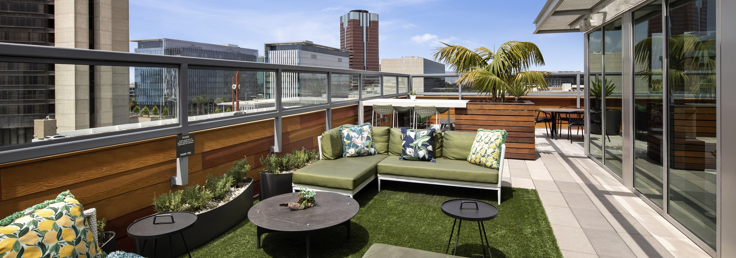 Exterior daytime view of landscaped rooftop lounge with comfortable seating area with pillows and tables overlooking the city