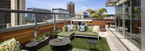 Exterior daytime view of landscaped rooftop lounge with comfortable seating area with pillows and tables overlooking the city