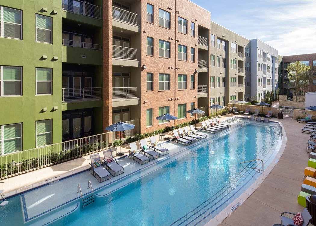 Exterior view of pool at AMLI at Mueller with blue umbrellas and white lounge chairs with facing building facade