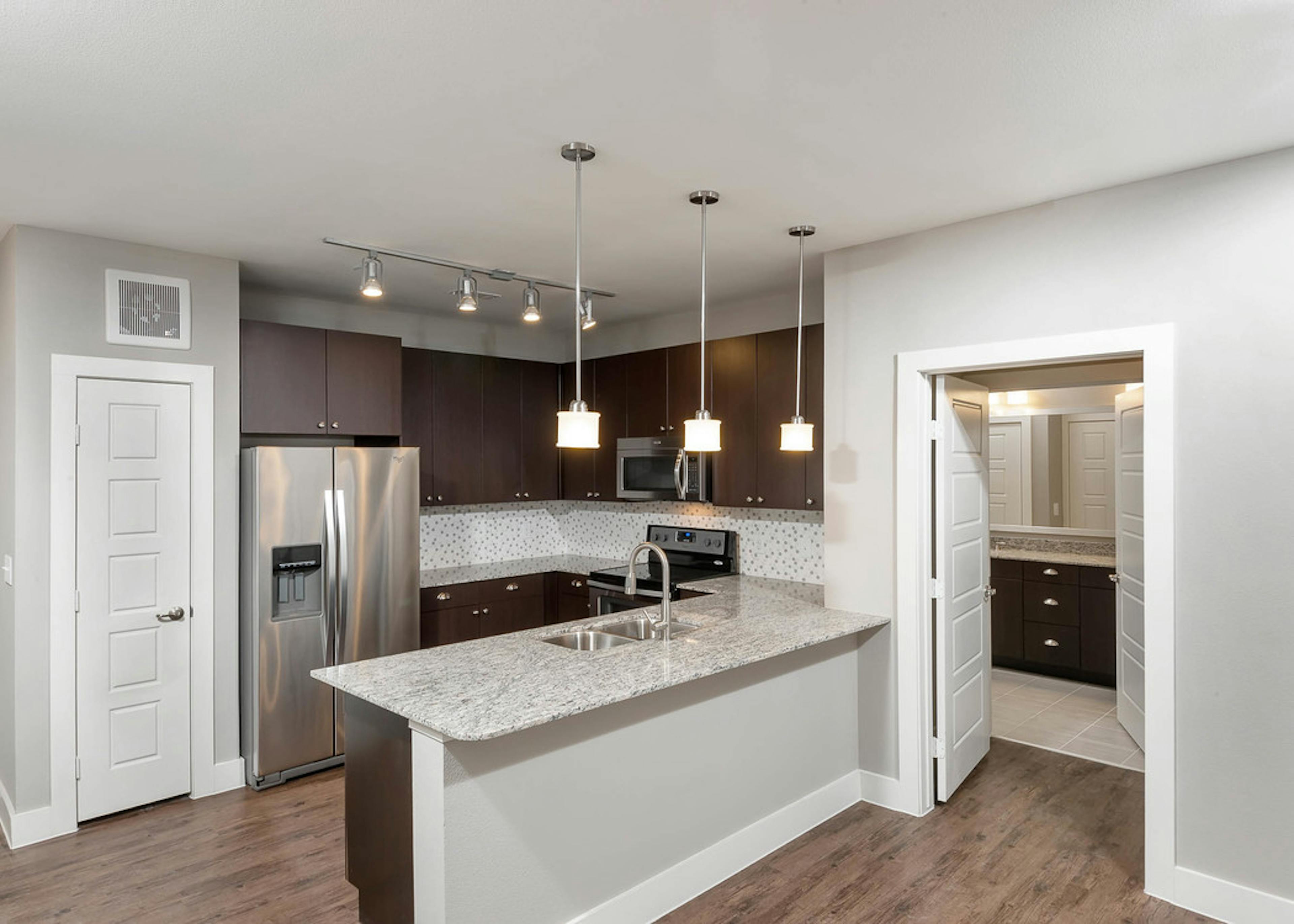 Interior of AMLI Frisco Crossing apartment kitchen with espresso cabinetry and tile backsplash and stainless steel appliances