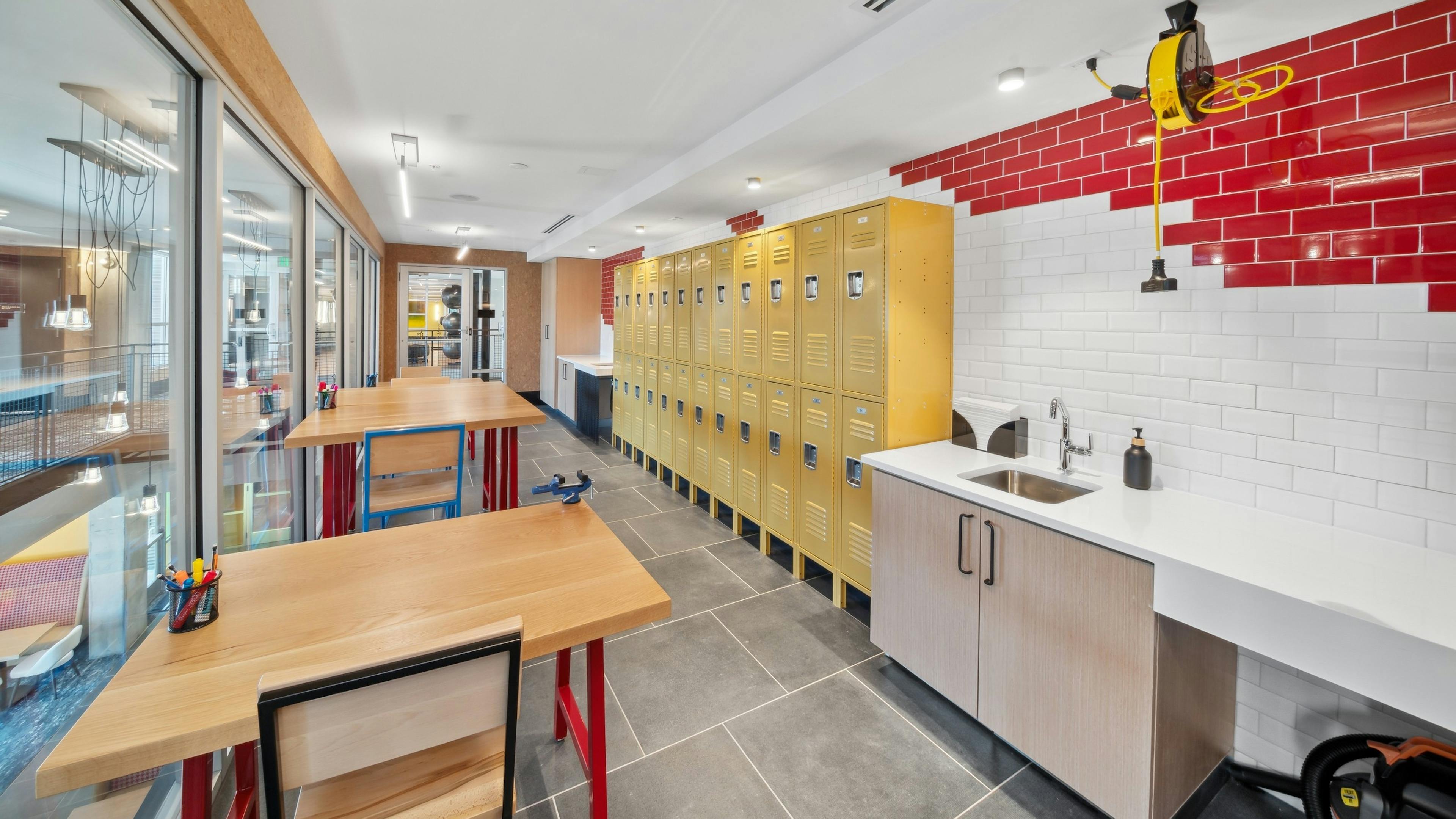 Maker space at AMLI RiNo with white and red tile wall and yellow lockers with counter and sink area and high tables and chairs