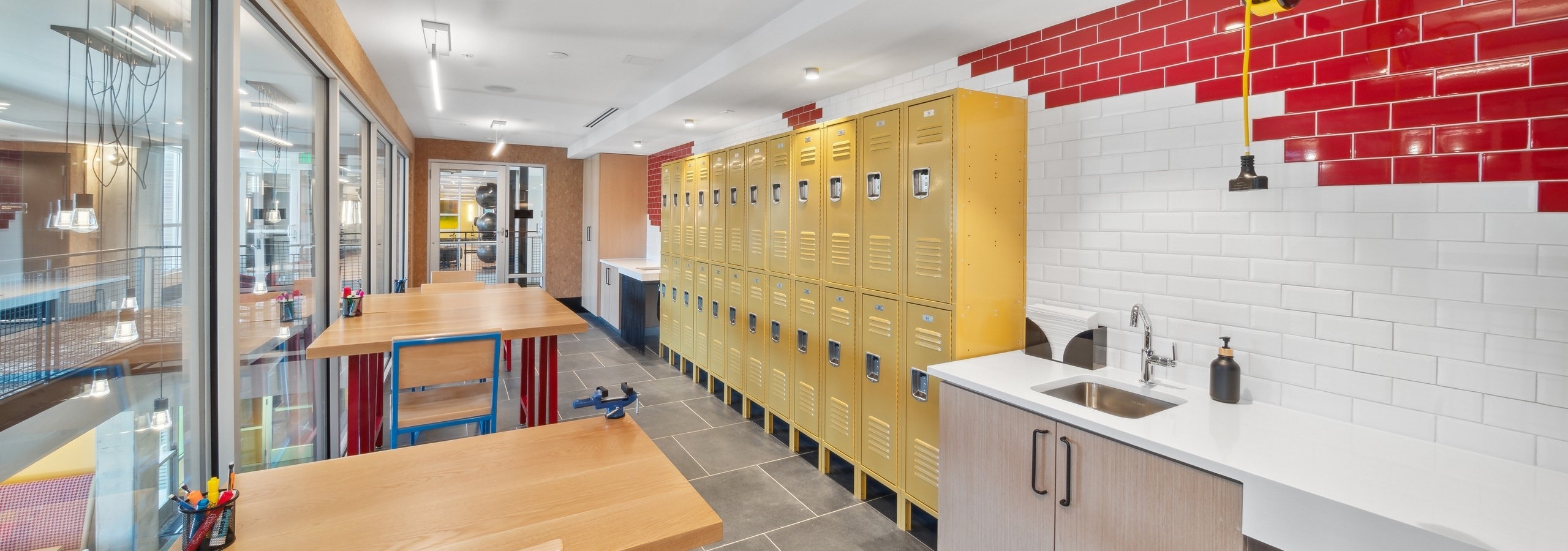 Maker space at AMLI RiNo with white and red tile wall and yellow lockers with counter and sink area and high tables and chairs