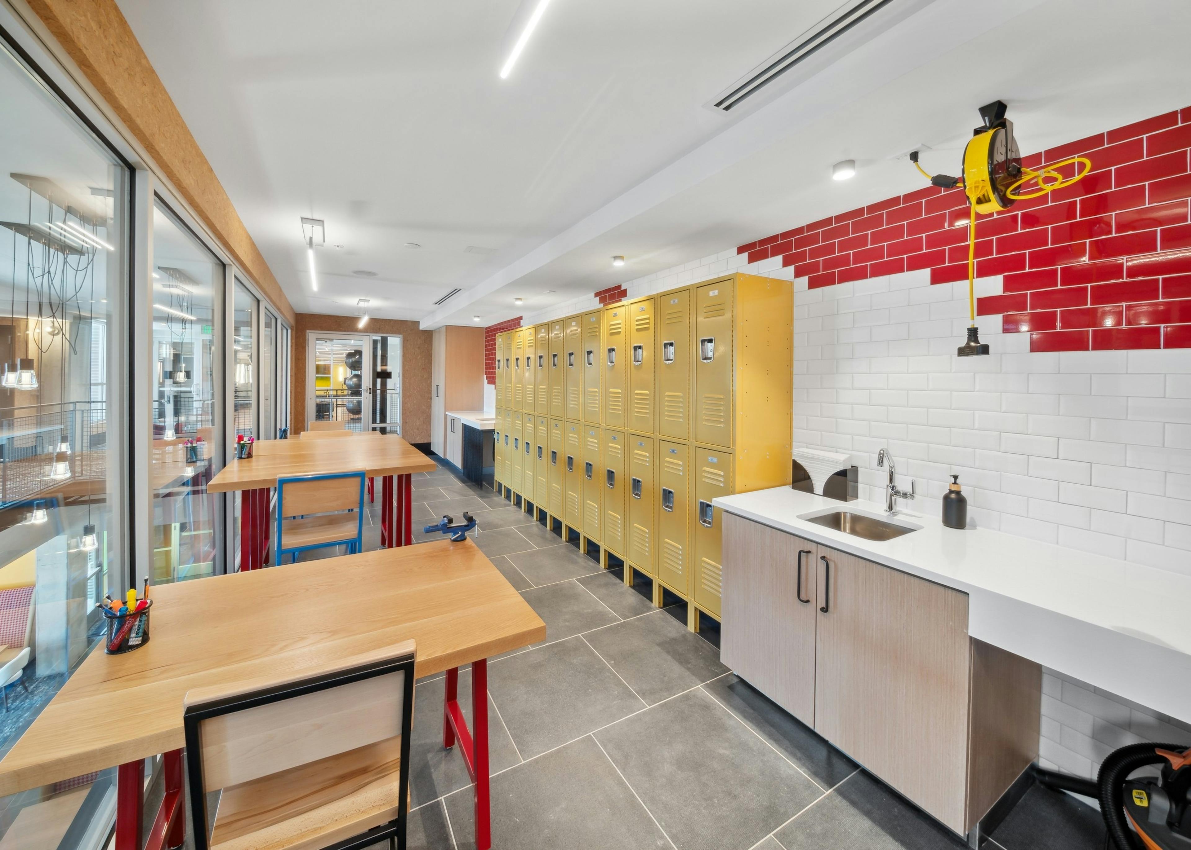 Maker space at AMLI RiNo with white and red tile wall and yellow lockers with counter and sink area and high tables and chairs