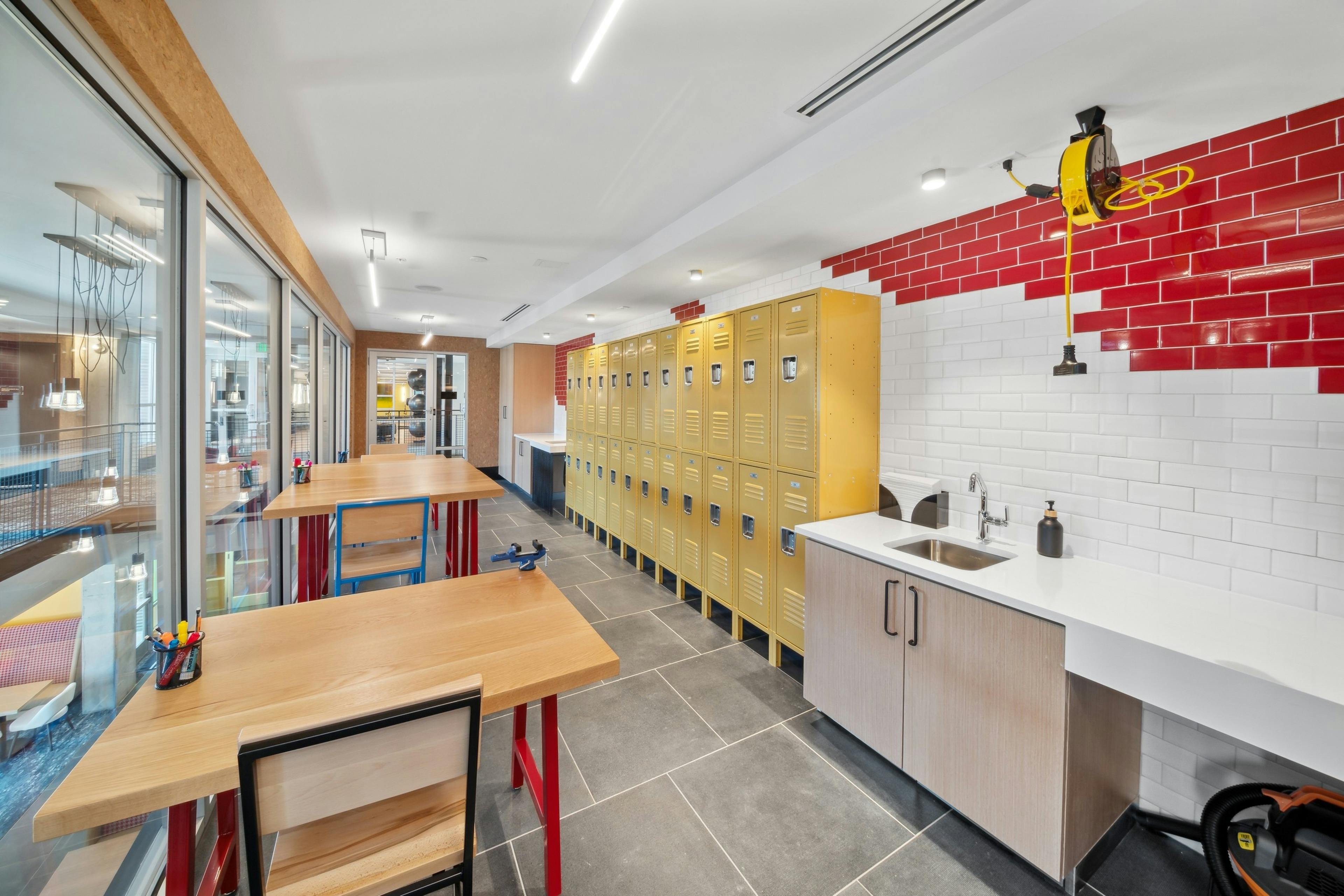 Maker space at AMLI RiNo with white and red tile wall and yellow lockers with counter and sink area and high tables and chairs