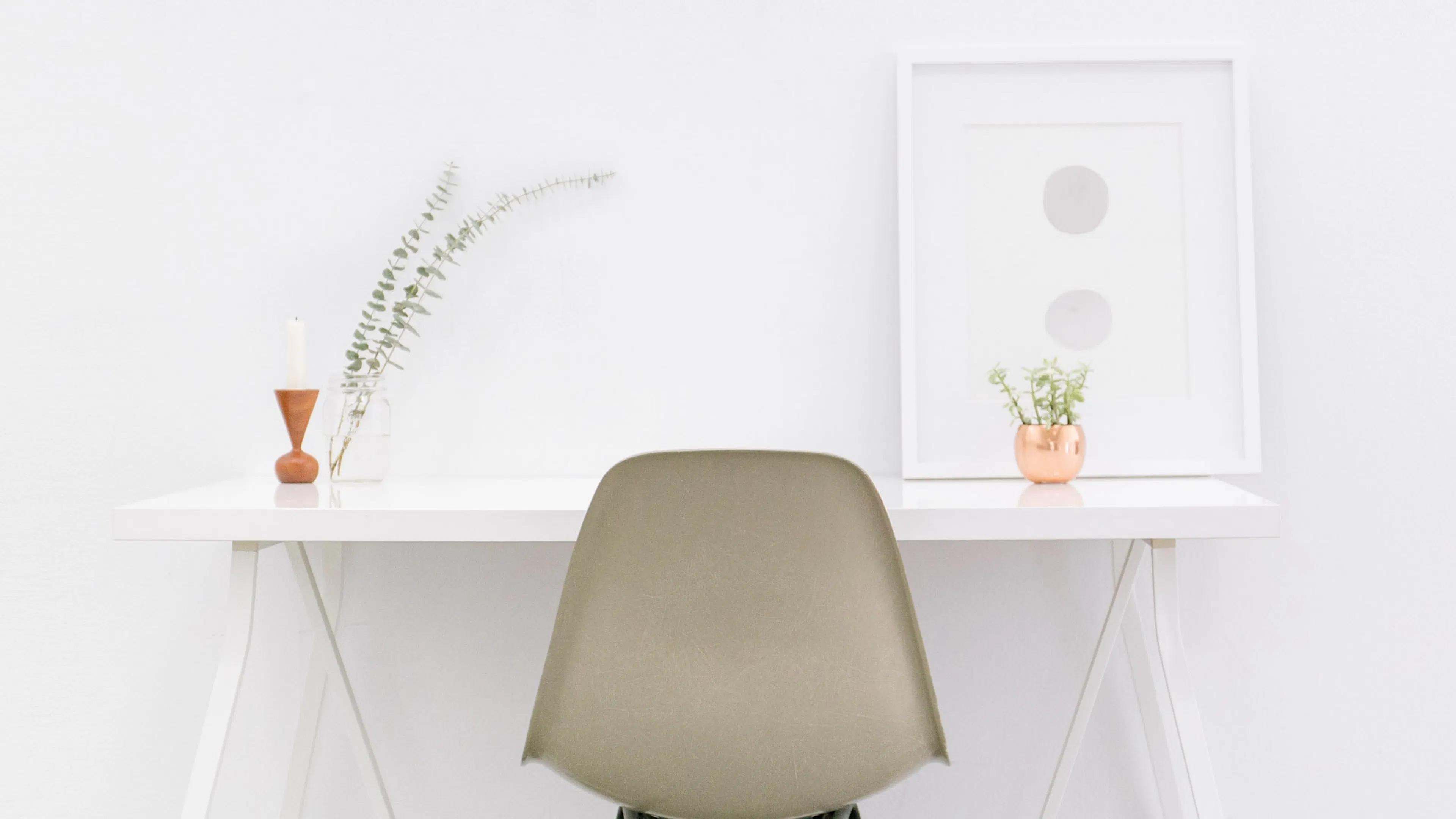 white desk and chair against a bare wall with a small plant sitting on the desk