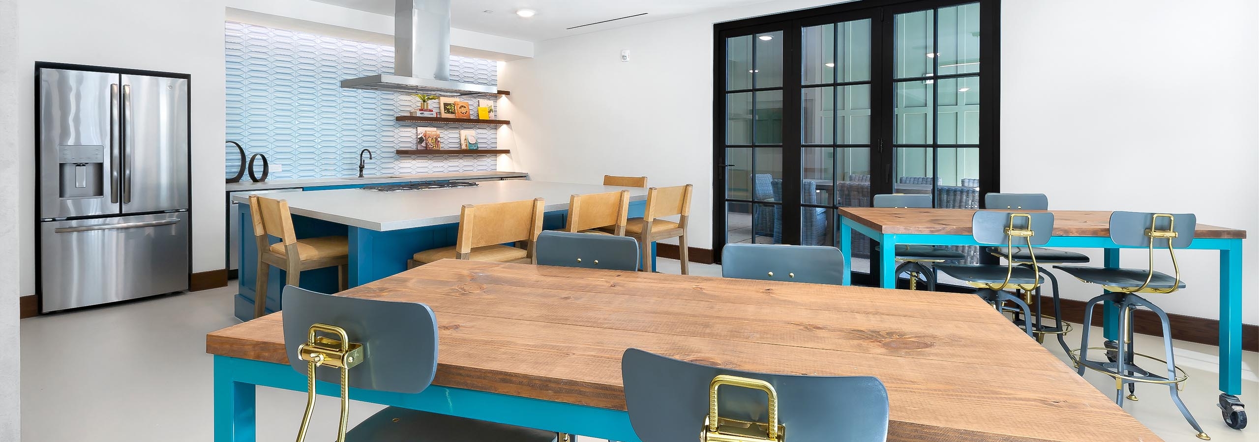 Interior view of resident kitchen with stainless steel appliances and three tables with chairs at AMLI Lakeline apartments